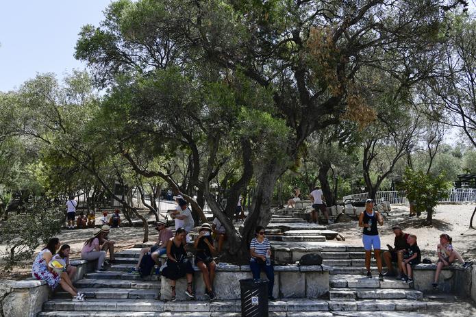 Turistas se resguardan del agobiante calor afuera de la antigua Acrópolis, en Atenas, Grecia, el 3 de agosto de 2021. Los termómetros en la capital griega han llegado a 42 grados. (AP Foto/Michael Varaklas)