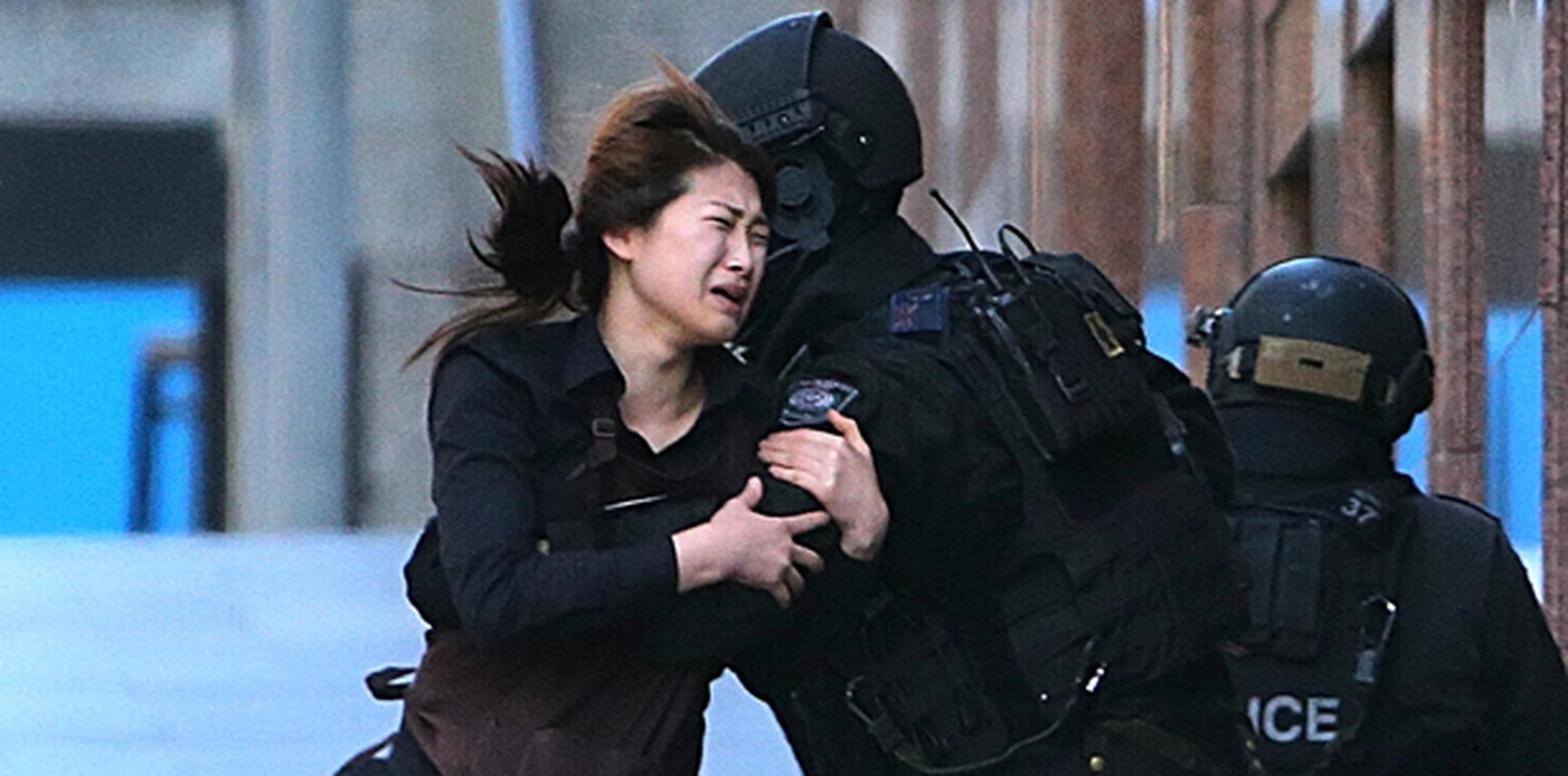 Una de las empleadas del establecimiento Lindt Chocolat Café corre hacia los agentes de la policía australiana tras lograr escapar seis horas después de que comenzara la crisis. (AP)
