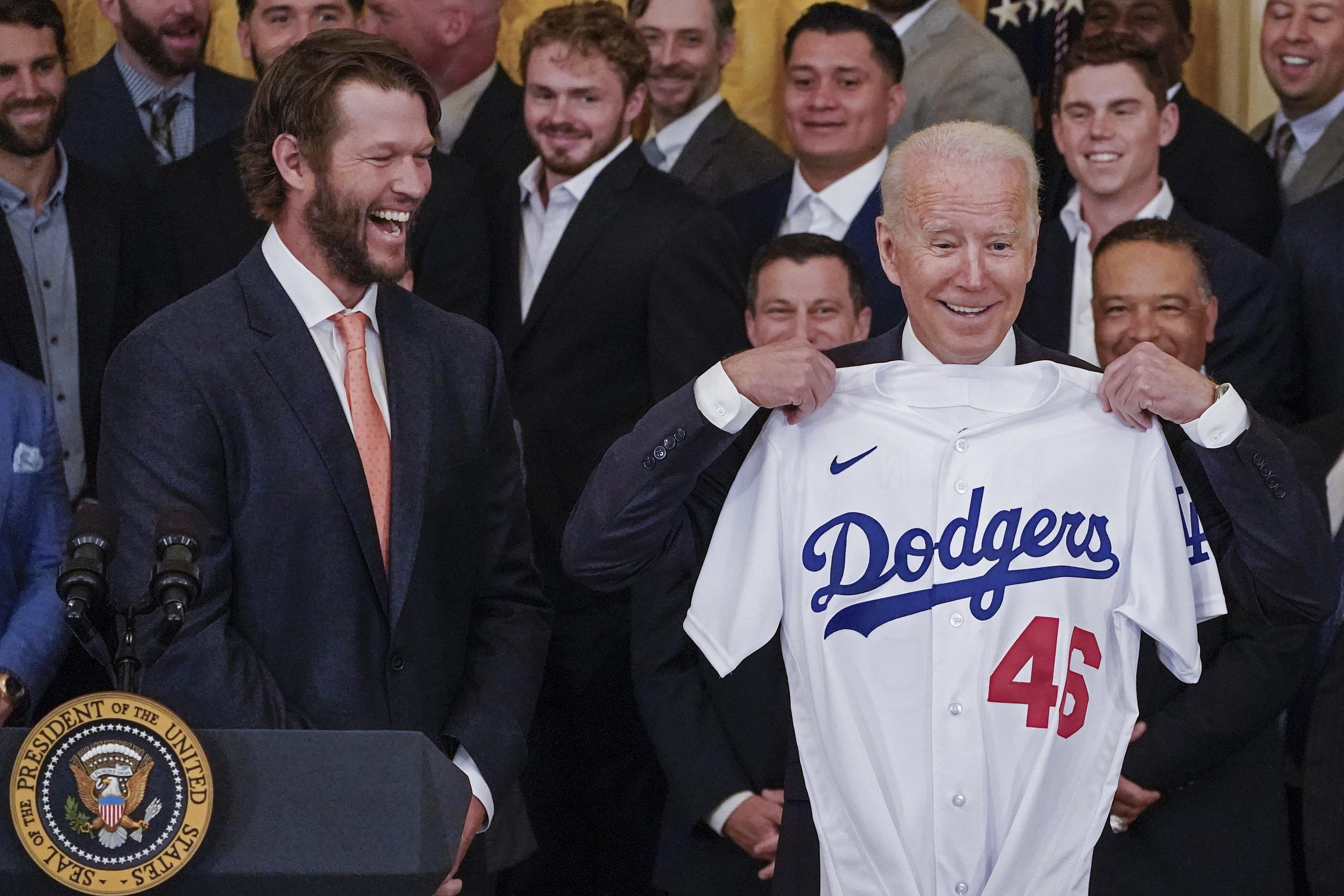 El as de los Dodgers de Los Angeles, Clayton Kershaw, reacciona mientras el presidente Joe Biden levanta la camisa de los Dodgers que le fue obsequiada durante la ceremonia del viernes.