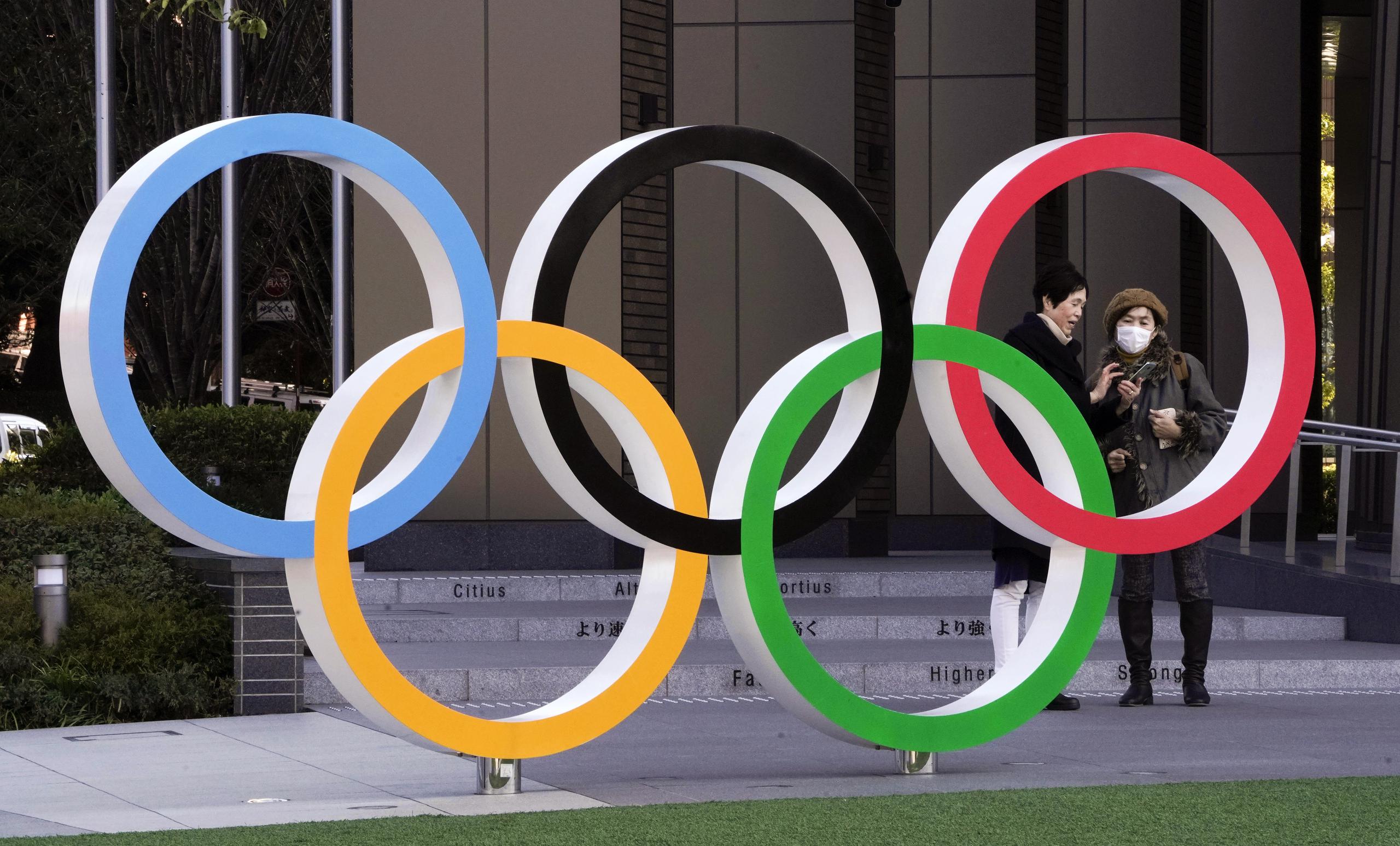 Dos japonesas, una de ellas con mascarilla, posan junto a las anillas olímpicas en Tokio.