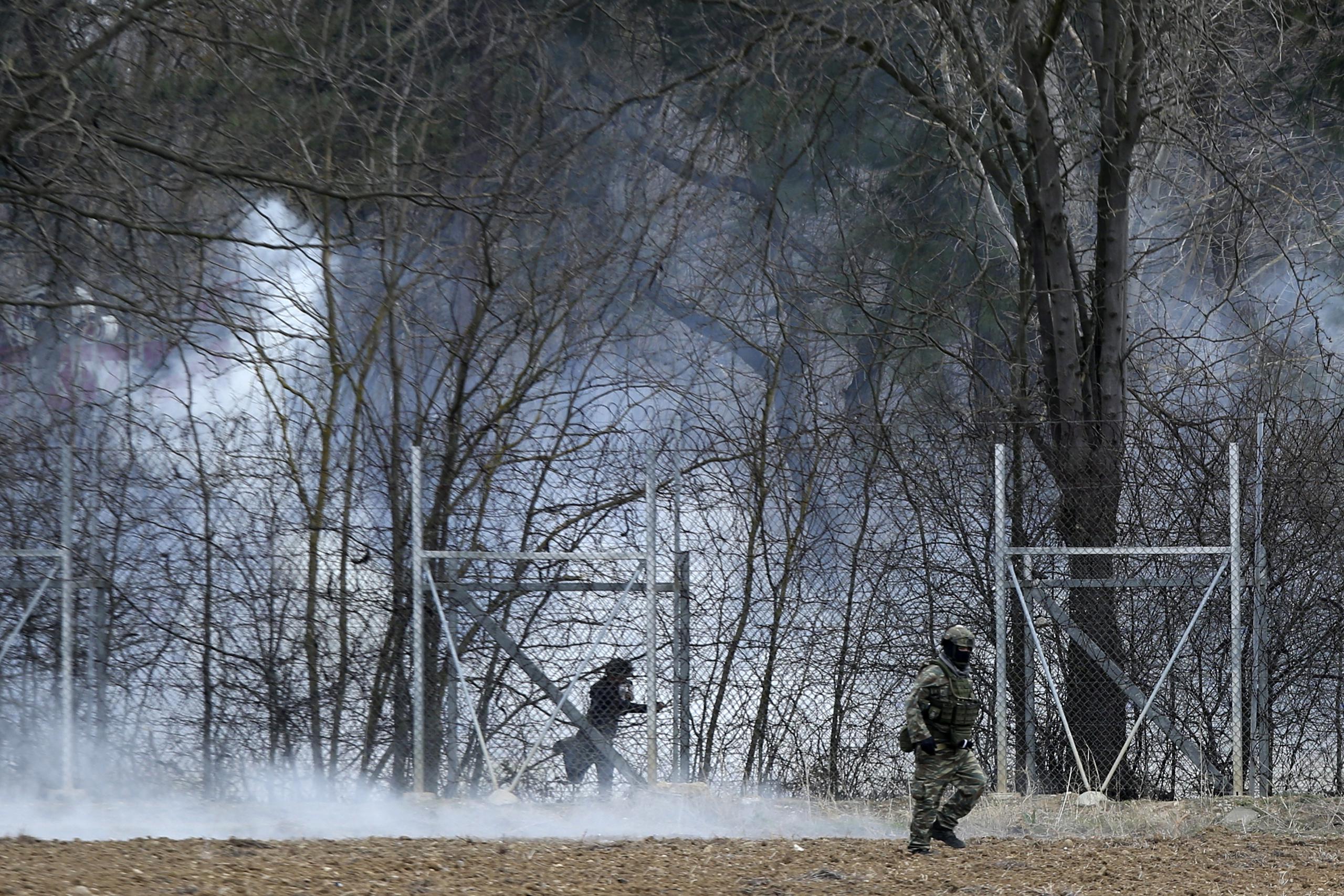 A Greek army officer patrols as a migrant is seen at the Turkish side at the Greek-Turkish border in Kastanies on Wednesday, March 4, 2020. Facing a potential wave of nearly a million people fleeing fighting in northern Syria, Turkey has thrown open its borders with Greece to thousands of refugees and other migrants trying to enter Europe, and has threatened to send "millions" more. (AP Photo/Giannis Papanikos)
