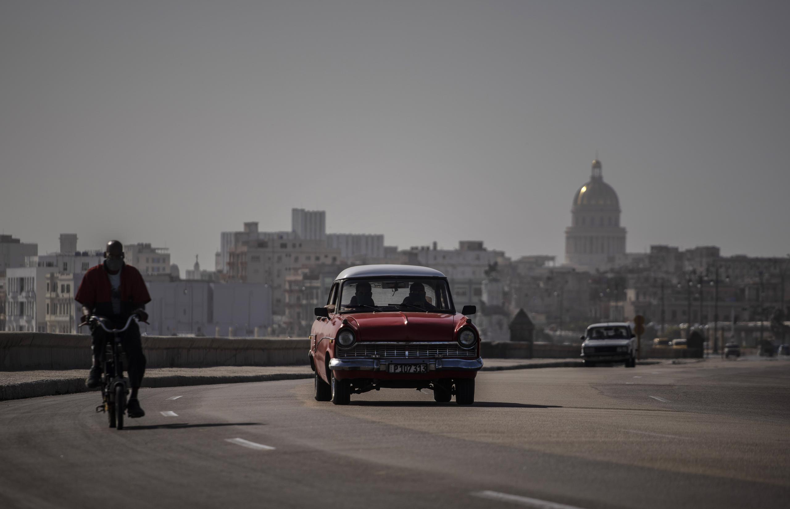 Un automóvil y una bicicleta clásicos estadounidenses comparten el camino en el Malecón en medio de una nube de polvo del Sahara en La Habana, Cuba.