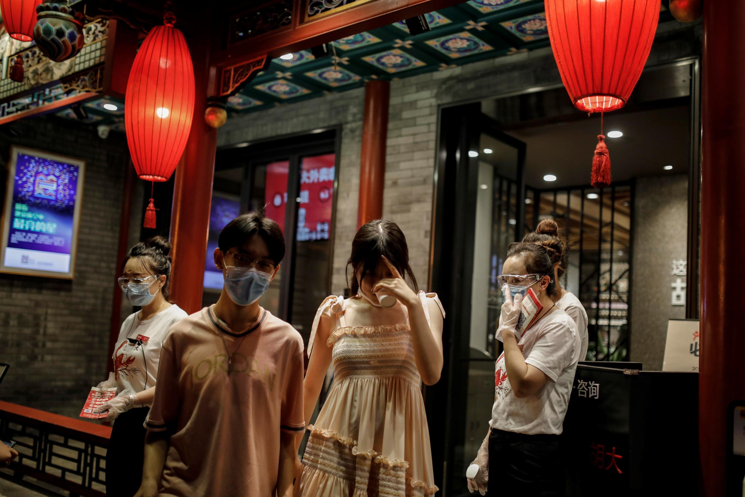 Personas con mascarillas salen de un restaurante en medio de la pandemia del coronavirus después de que se detectaran nuevos casos de COVID-19 en los últimos días en Pekín, China.