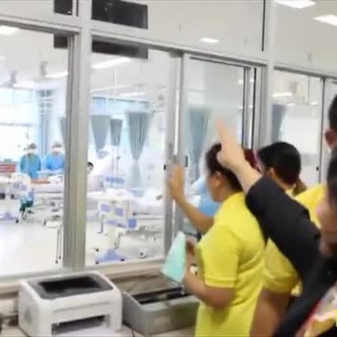 Niños tailandeses saludan a sus padres a través de un cristal