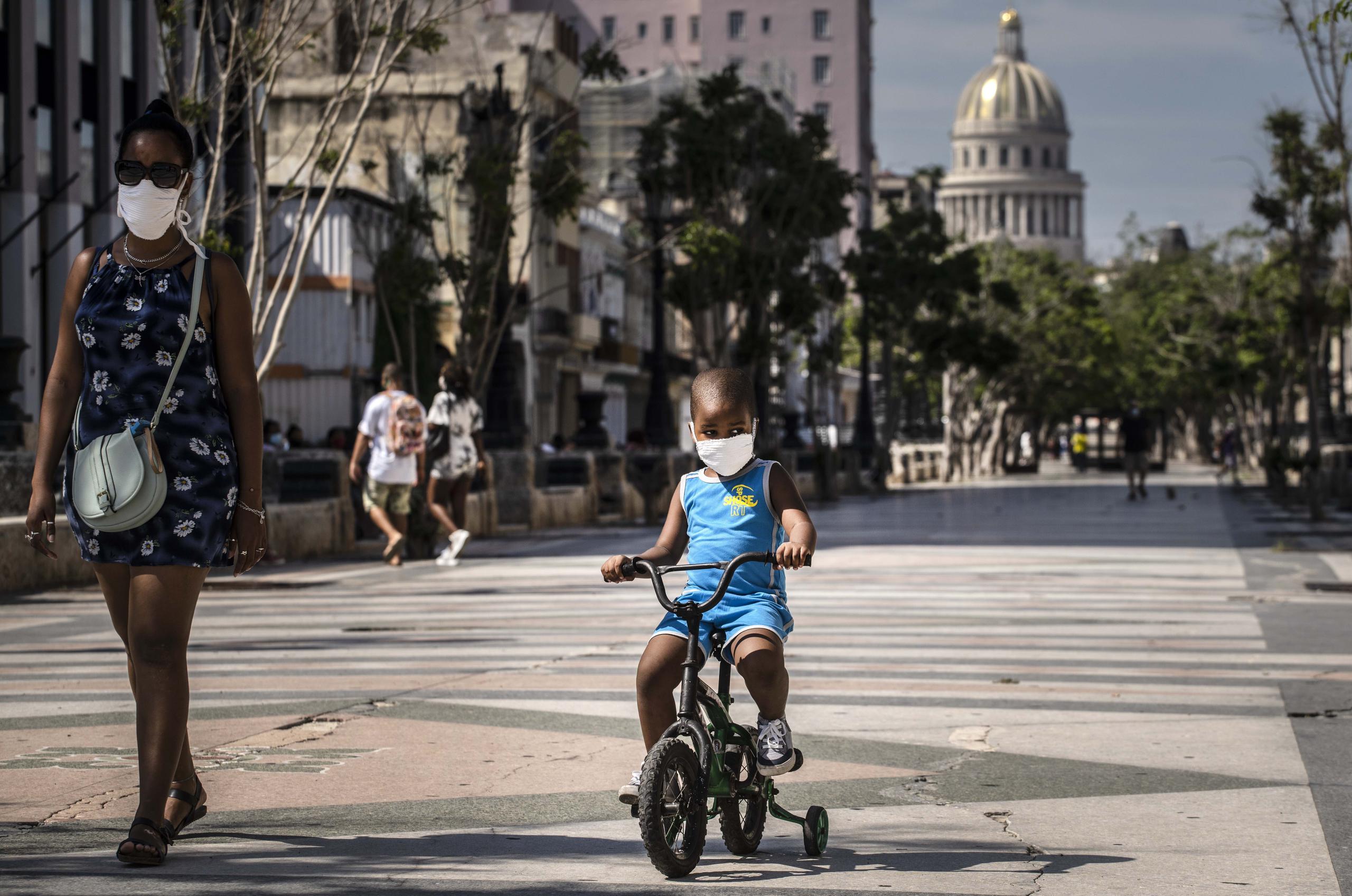 Una mujer acompaña a un niño en bicicleta, ambos con mascarillas protectoras como medida de precaución en medio de la propagación del nuevo coronavirus, en La Habana, Cuba.