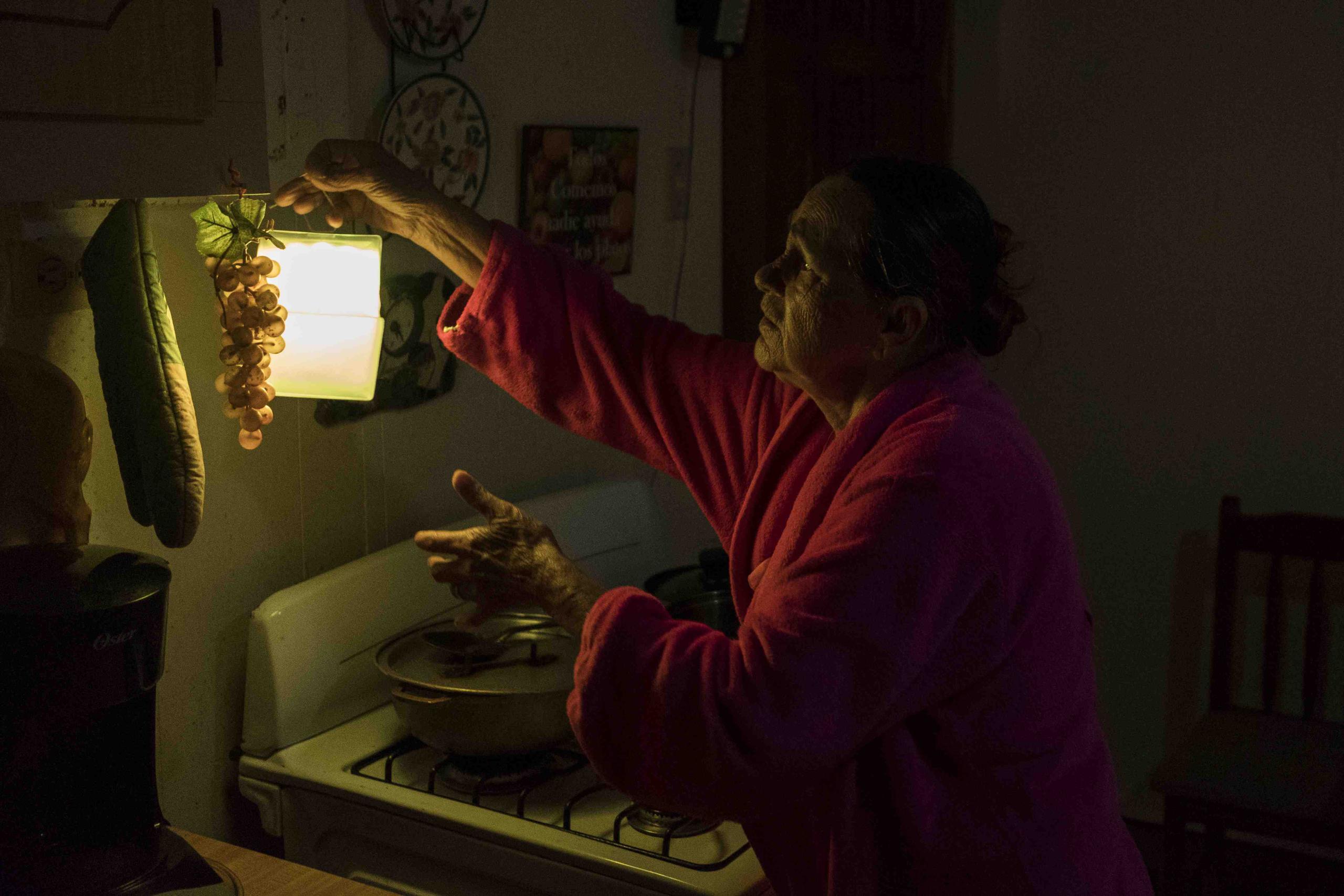 Marta Bermúdez Robles, de 66 años, cuelga una lámpara en su cocina, en Adjuntas, ante la falta de electricidad. (AP)