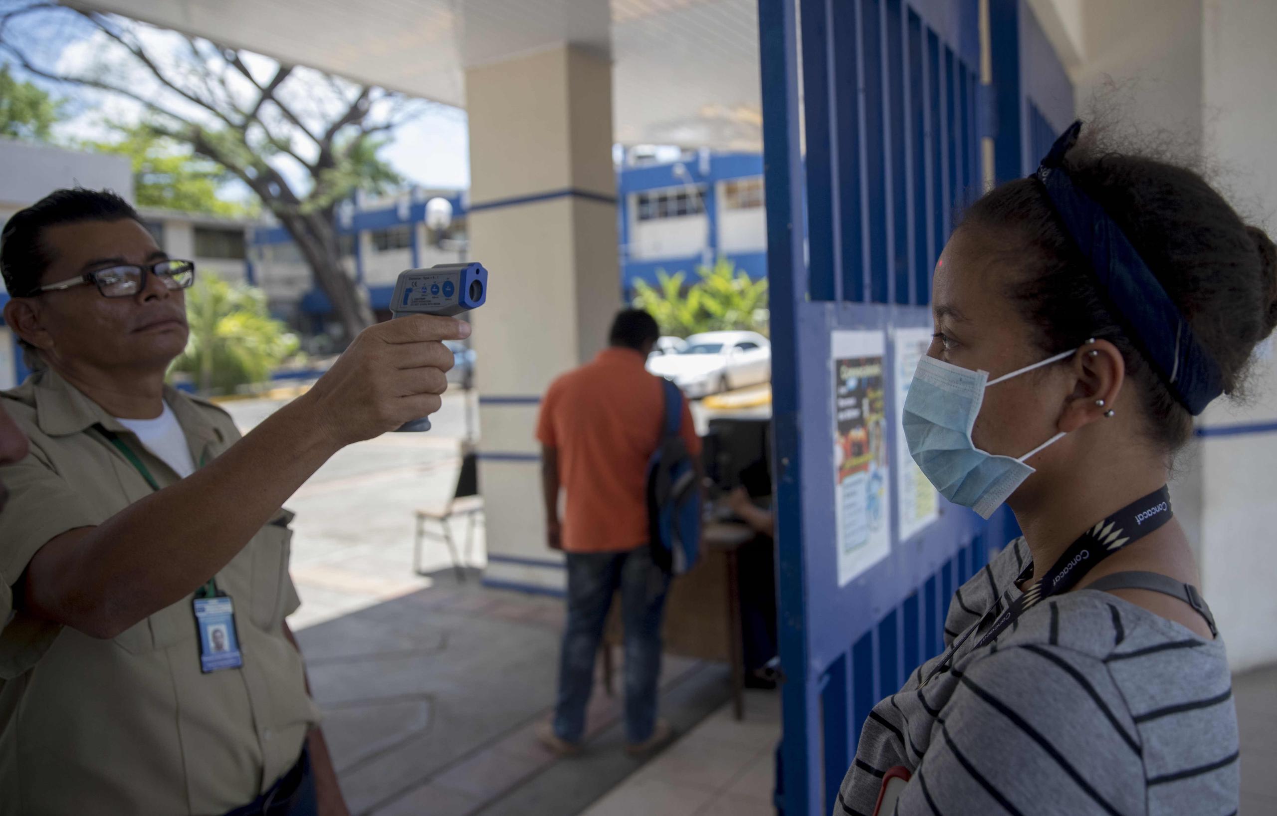 Un guarda de seguridad toma la temperatura a una mujer en la entrada de la Universidad Nacional de Ingeniería (UNI) en Managua, (Nicaragua).