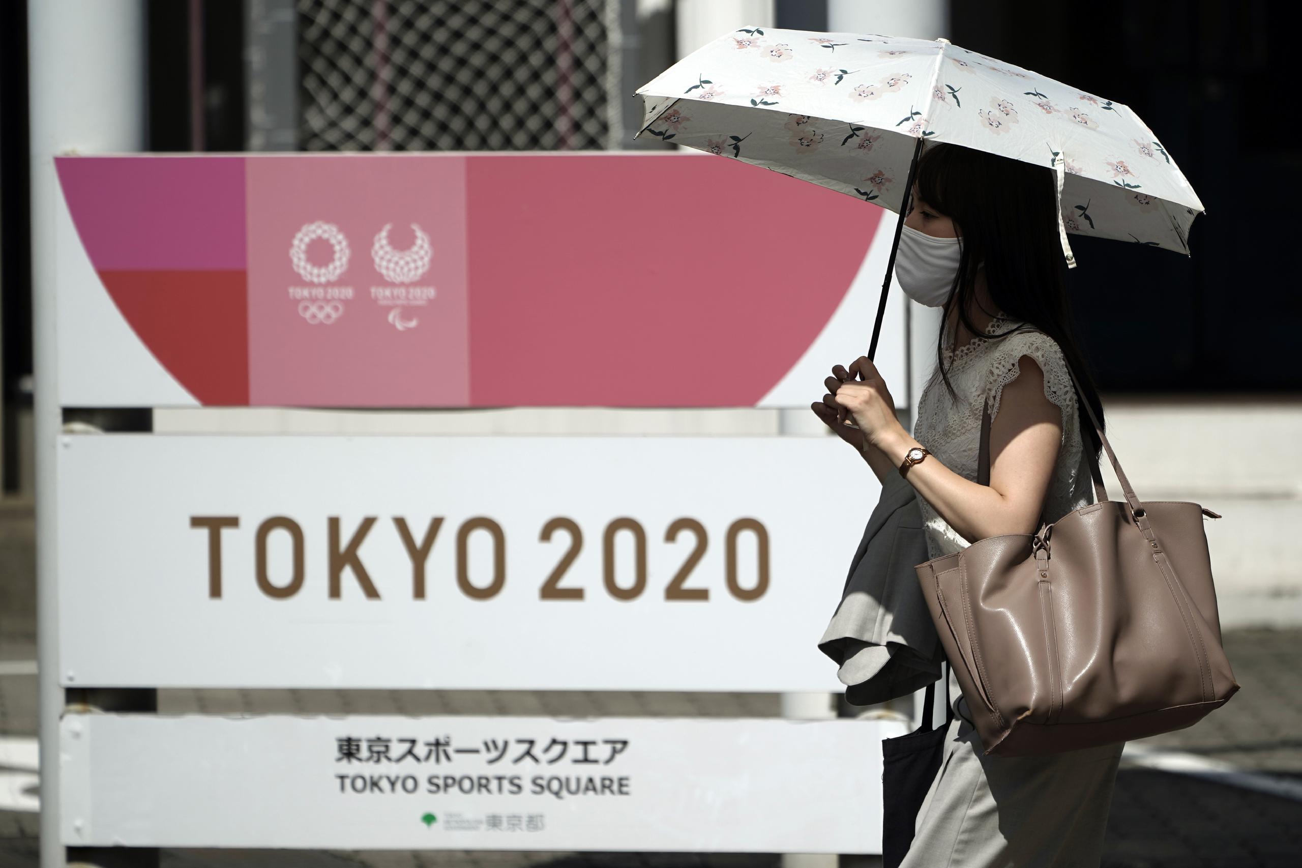 Una mujer con cubrebocas para frenar la propagación del coronavirus camina frente a un anuncio publicitario de los Juegos Olímpicos de Tokio.
