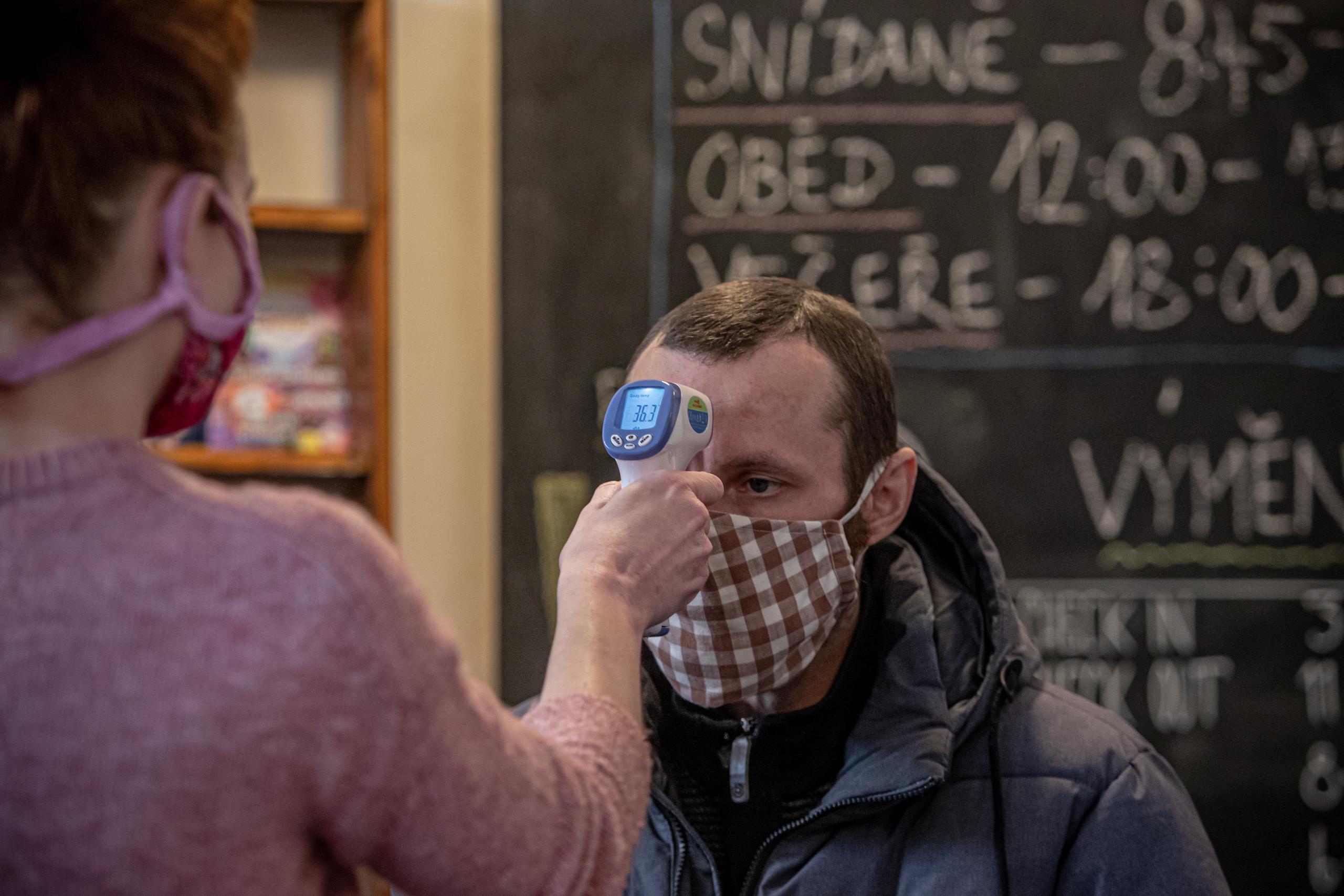 Una mujer con mascarilla le toma la temperatura a un hombre en la recepción de un albergue en Praga.