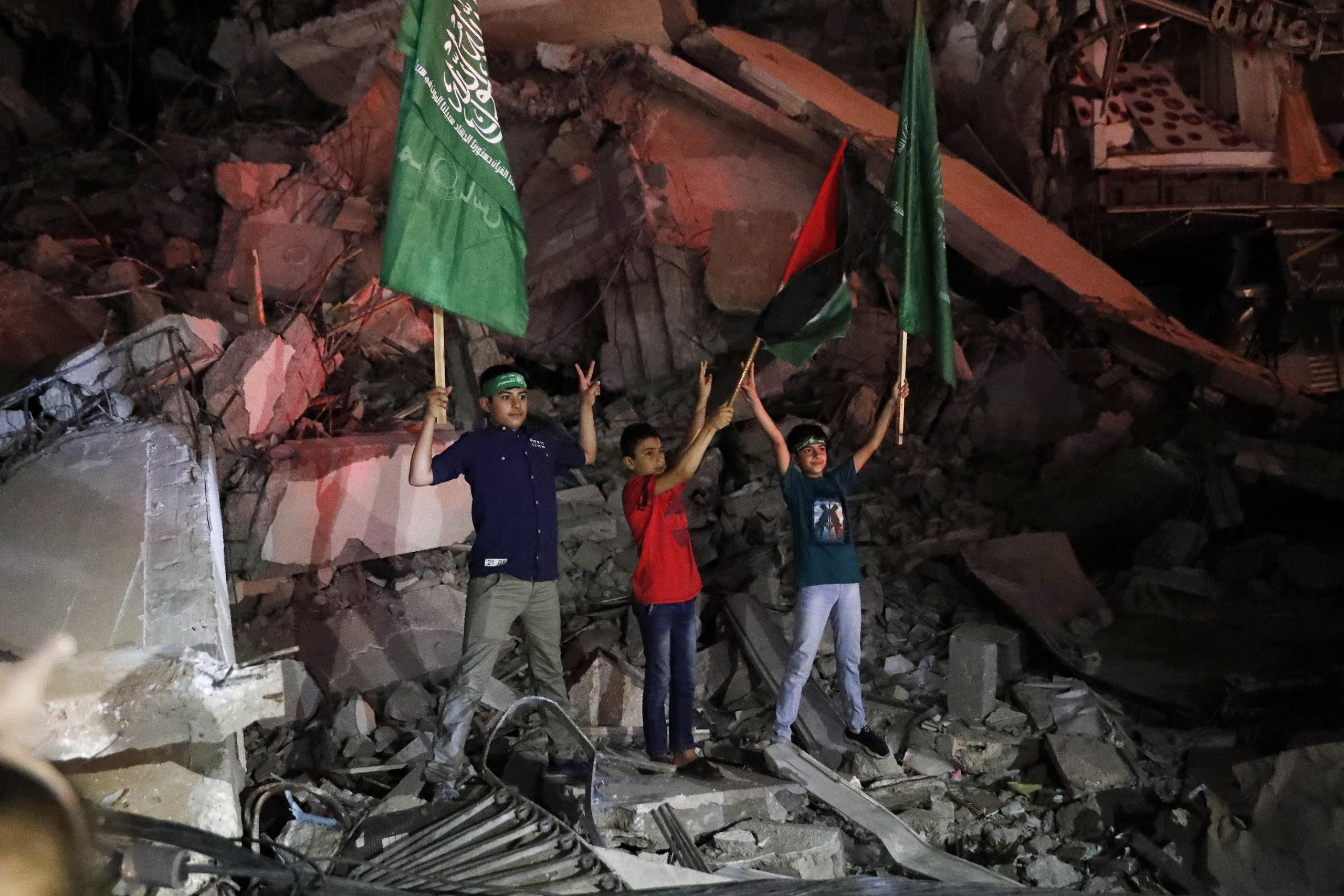 Niños palestinos ondean la bandera verde de Hamas y la palestina sobre los escombros de un edificio derribado mientras celebran el acuerdo de alto el fuego entre Israel y el grupo insurgente, en la Ciudad de Gaza.