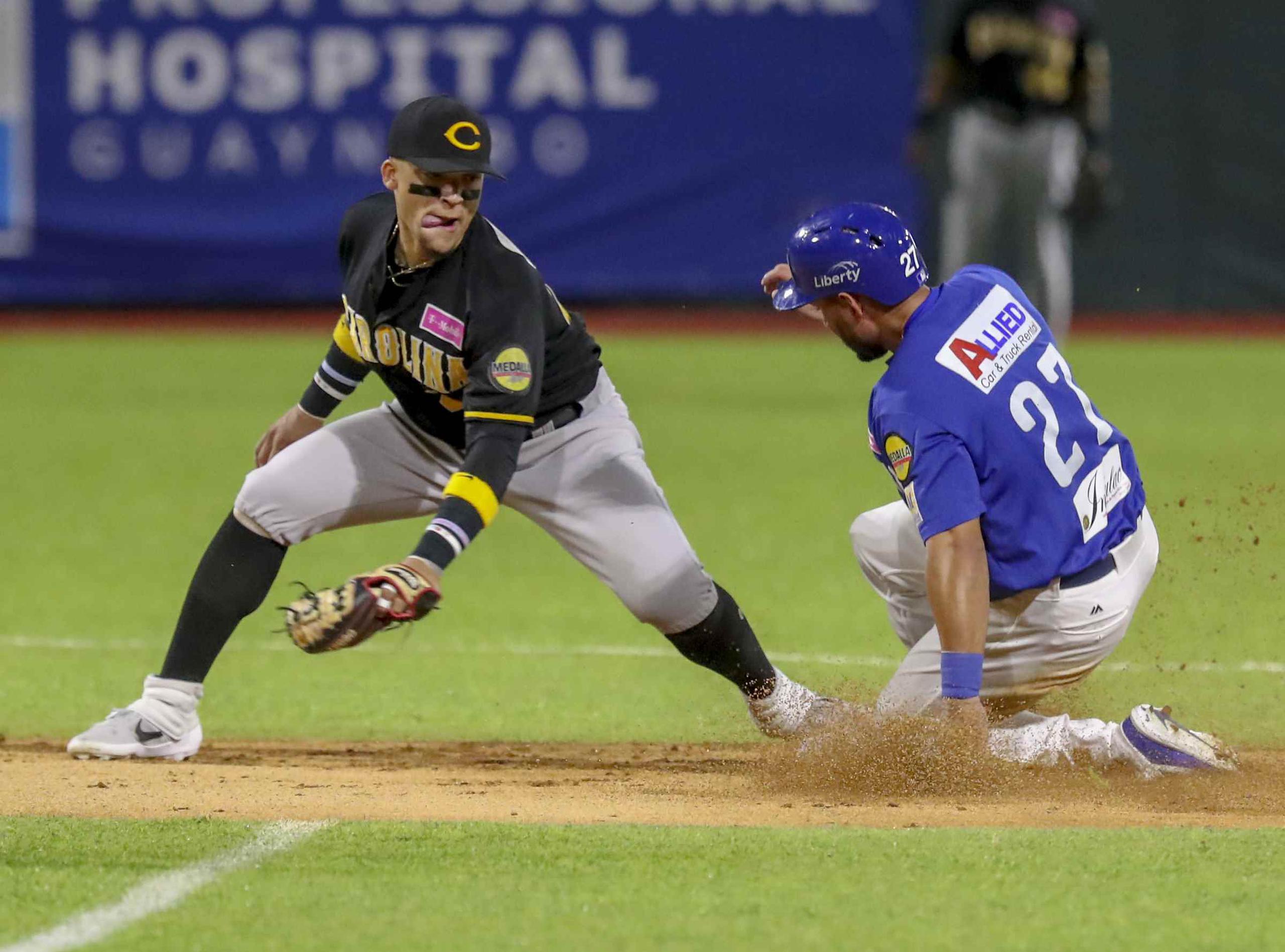 El lanzador de Carolina, Isan Diaz (a la izquierda) y intenta detener al jugador de Santurce, Raymound Fuentes, mientras llega a salvo a la segunda base.