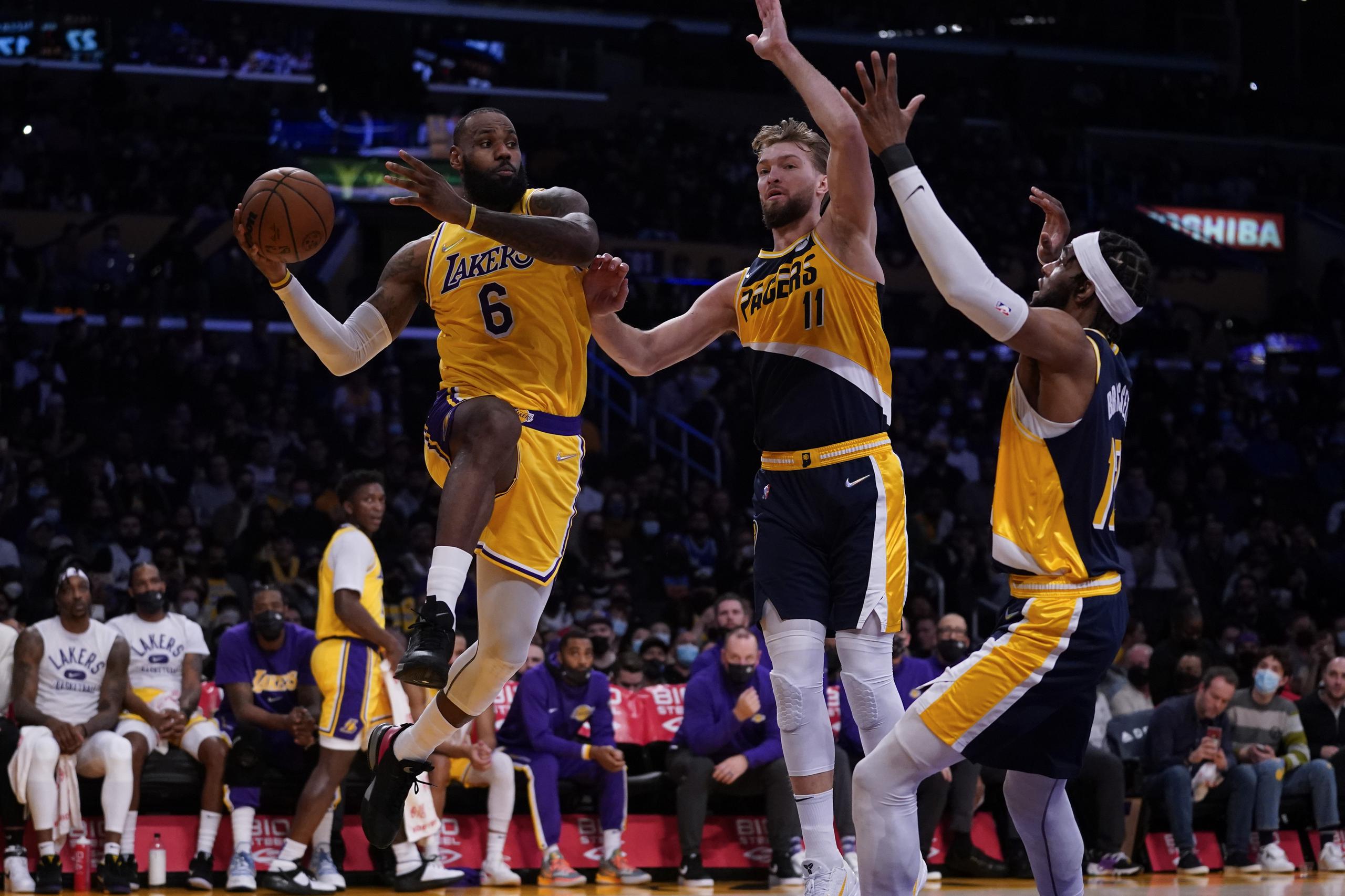 LeBron James (6), de los Lakers de los Ángeles, realiza un pase ante la presión de los jugadores de los Pacers de Indiana Domantas Sabonis (11) y Oshae Brissett (12) en la primera mitad del juego de la NBA que enfrentó a ambos equipos en Los Ángeles, el 19 de enero de 2022.