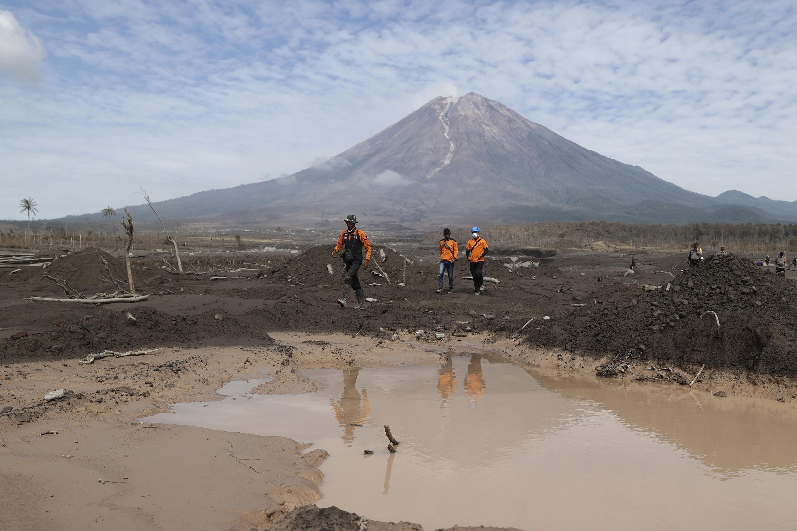 Socorristas caminan en un área afectada por la erupción del monte Semeru, al fondo, durante una búsqueda de víctimas en Lumajang, Java Oriental, Indonesia, el miércoles 8 de diciembre de 2021. (Foto AP/Trisnadi)