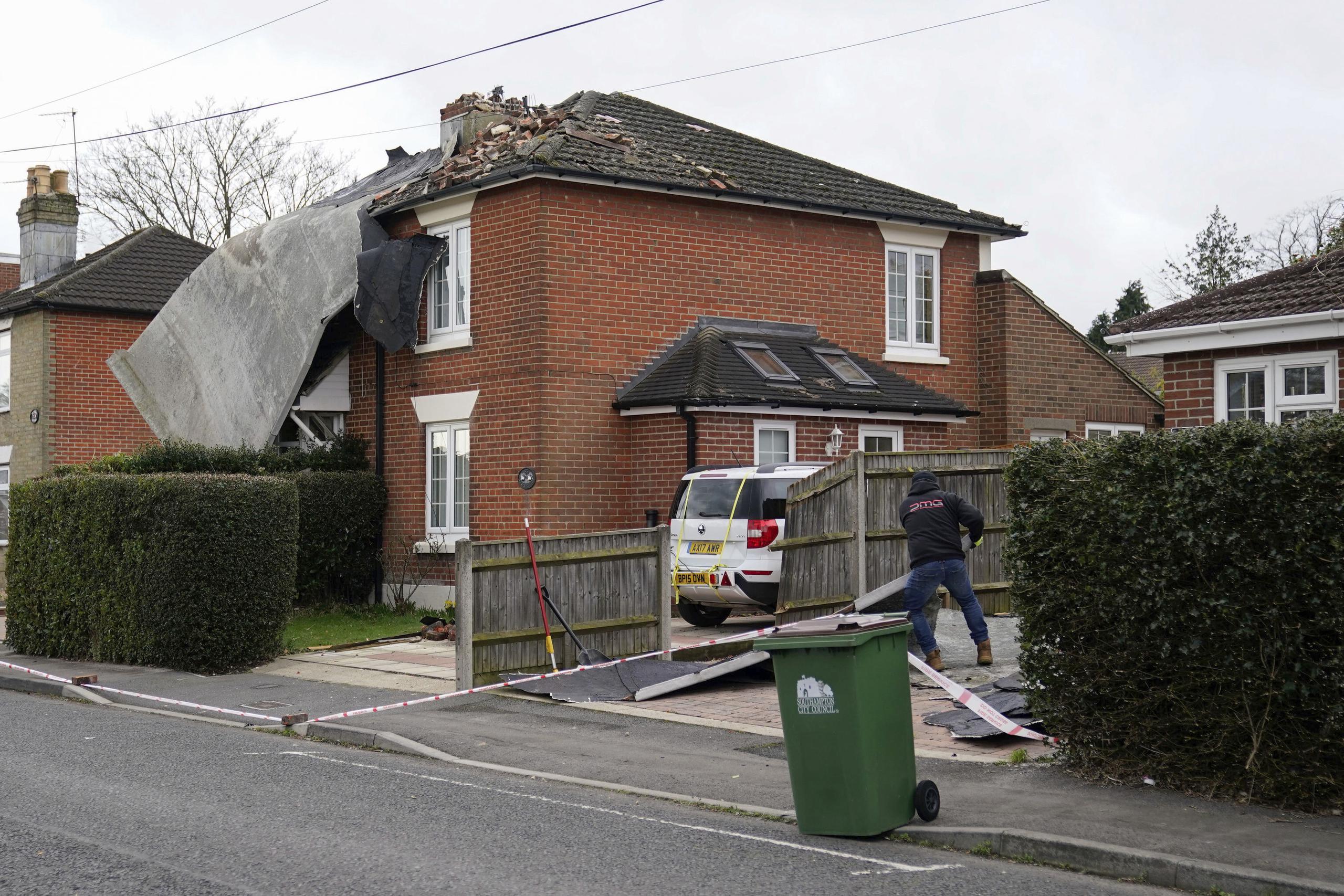 Un hombre limpia la entrada para el auto después de que un techo de un edificio de apartamentos cercano cayó sobre una casa en Bitterne, Southampton, Inglaterra, el sábado 19 de febrero de 2022. (Andrew Matthews/PA vía AP)