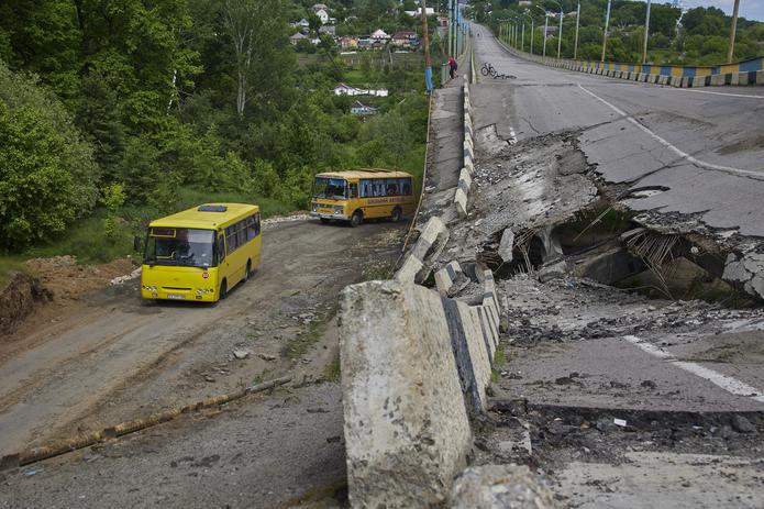 Varios autobuses escolares que transportan refugiados ucranianos pasan por un puente dañado cerca de Járkov, Ucrania. (EFE/EPA/SERGEY KOZLOV)