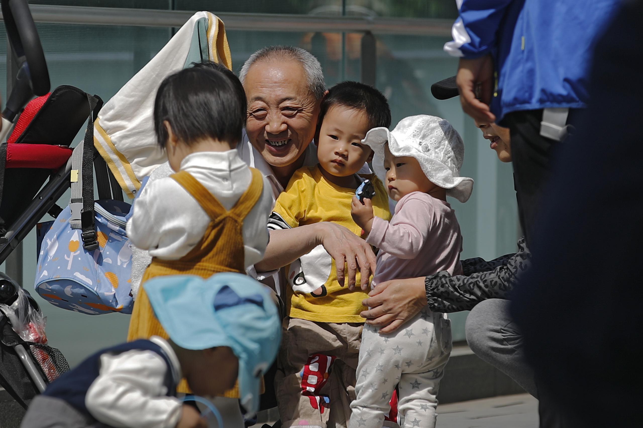 Un hombre mayor juega con niños cerca de un edificio de oficinas en Pekín. El gobierno chino relajará los límites de natalidad para permitir que todas las parejas puedan tener tres hijos en lugar de dos para hacer frente al rápido envejecimiento de la población.