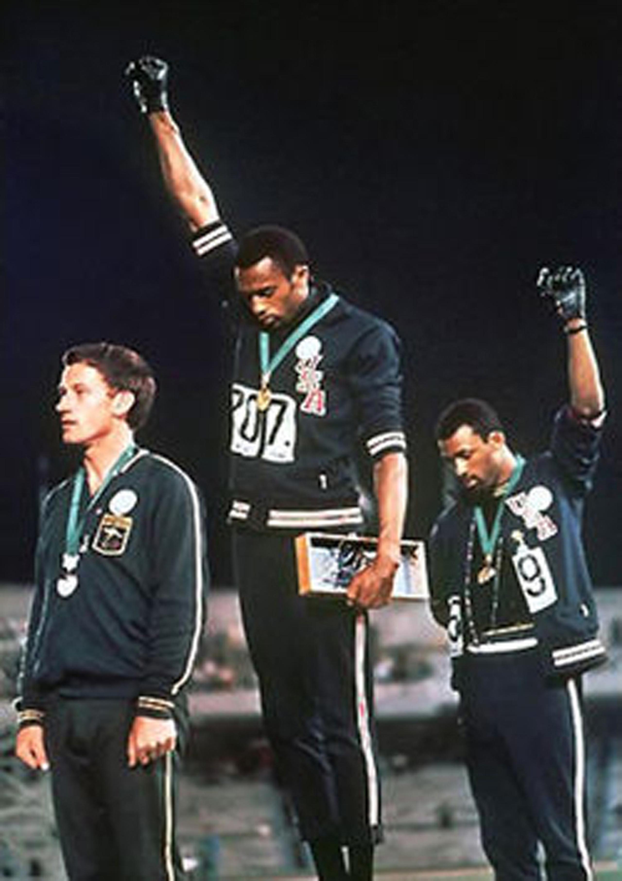 Tommie Smith (al centro) y John Carlos (derecha) hacen un saludo simbólico del movimiento Black Power durante las Olimpiadas México 1968, mientras que Peter Norman lleva una insignia apoyando el sentir de ambos corredores estadounidenses.