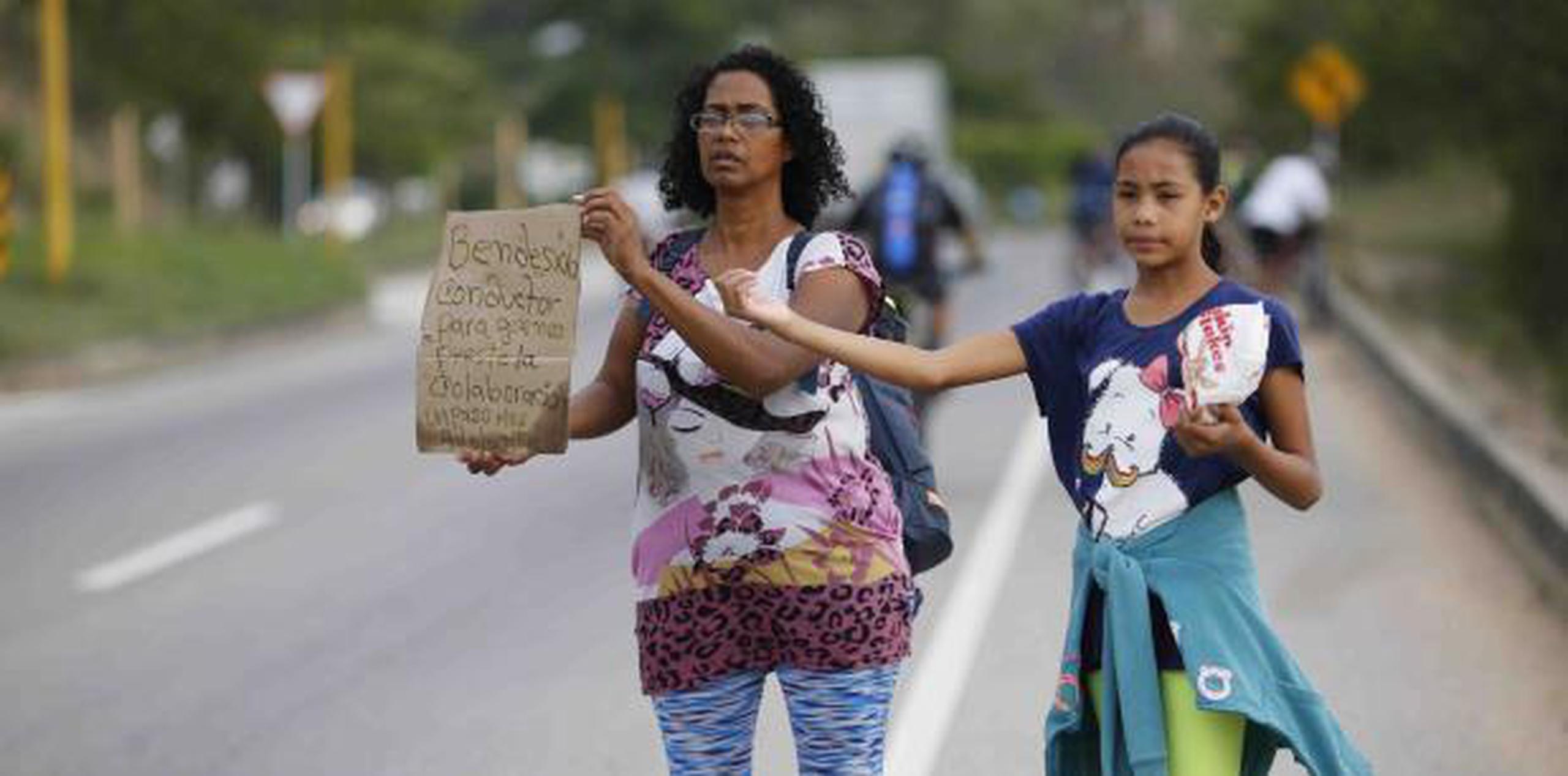 Sandra Cádiz sostiene un cartel hecho a mano con el mensaje "Bendesido (sic) conductor para que nos preste la colaboración", mientras su hija de 10 años, Angelis, espera con ella. (AP)