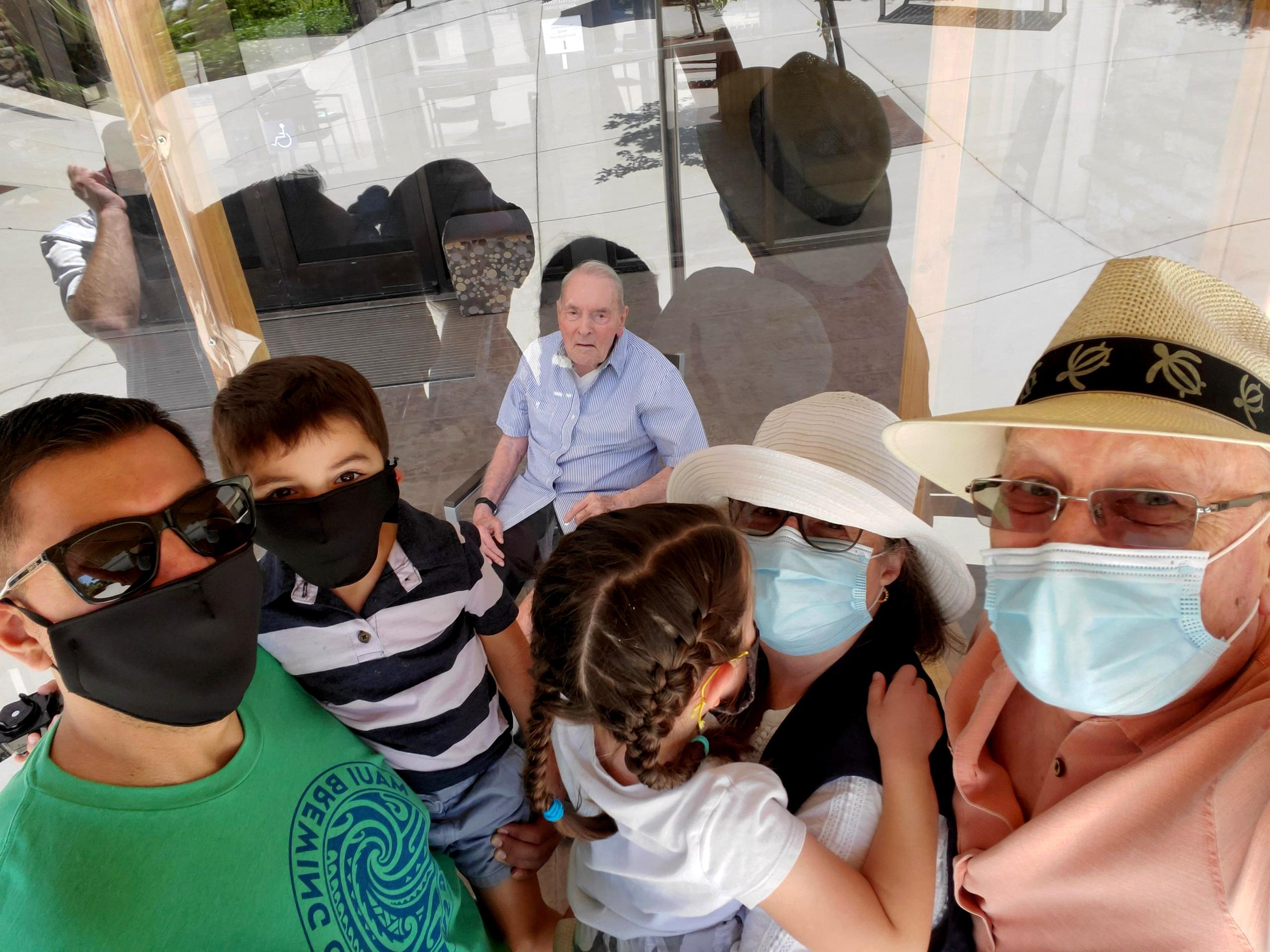 Wake Sharp, de 93 años, al centro y detrás del cristal, mientras es visitado por otras tres generaciones de su familia con motivo del Día del Padre en Fairfield, California