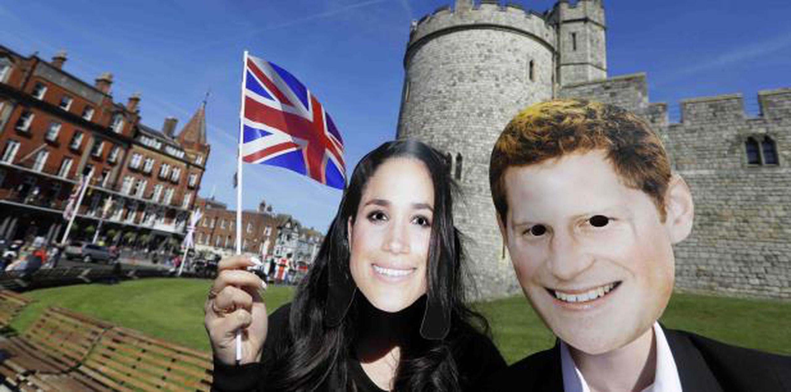 Una pareja con máscaras del príncipe Enrique y su prometida la actriz Meghan Markle posan frente al palacio de Windsor.  (AP)
