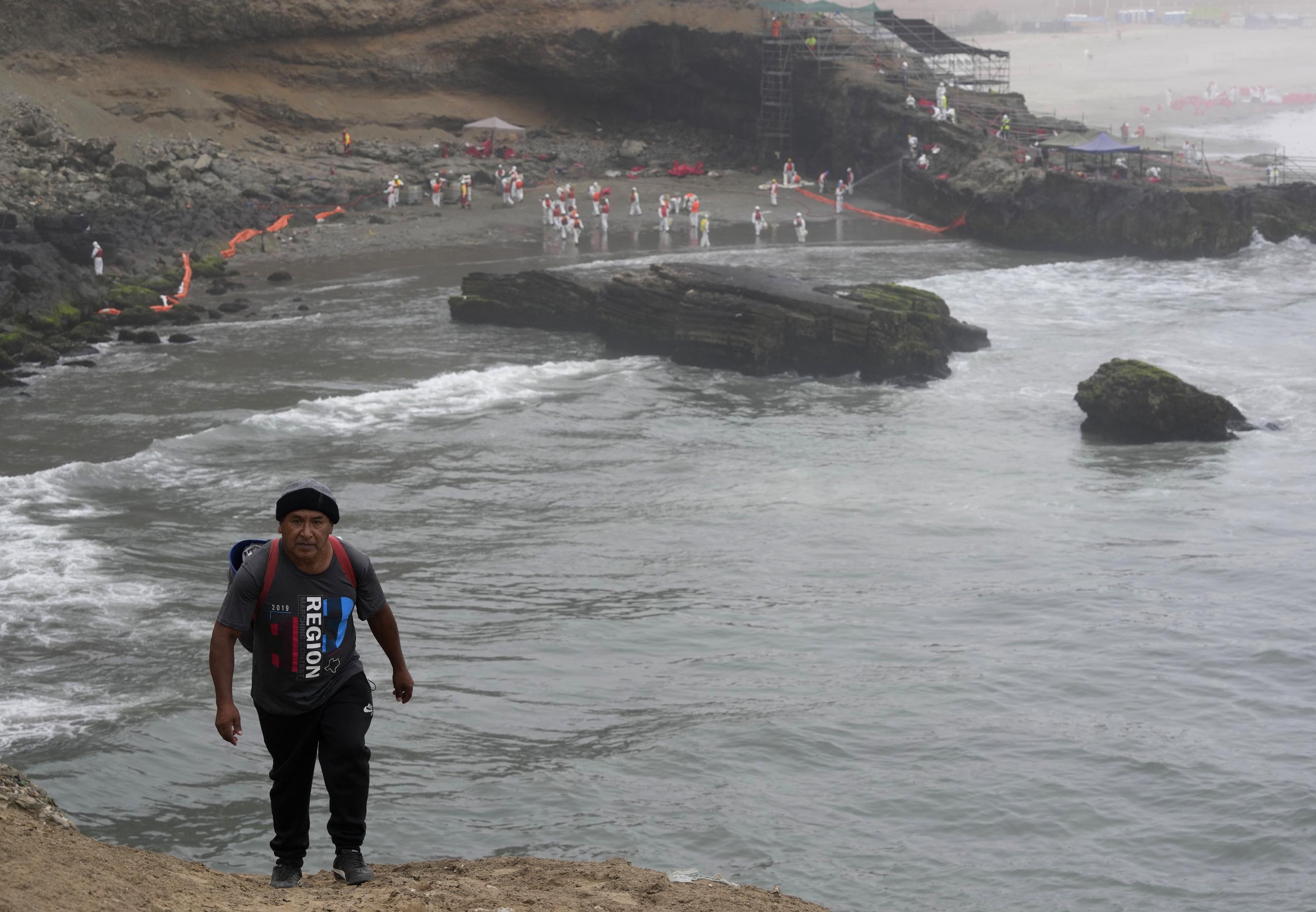 El pescador Walter de la Cruz se aleja con las manos vacías, mientras los trabajadores continúan en una campaña de limpieza de petróleo en la playa Lluvia en el distrito de Ventanilla del Callao, Perú.