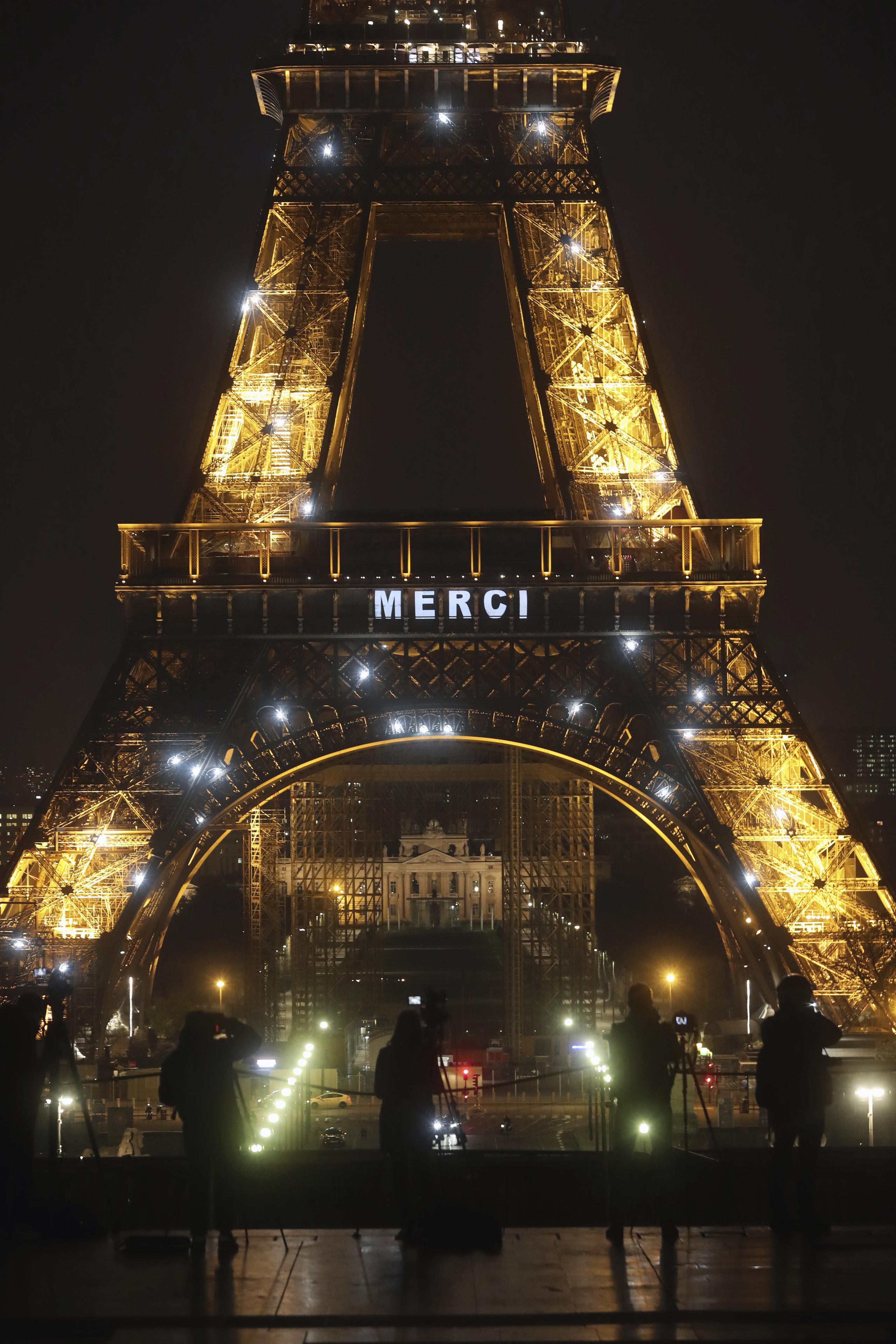 Miembros de la prensa apostados frente a la Torre Eiffel, que despliega la palabra "Merci"