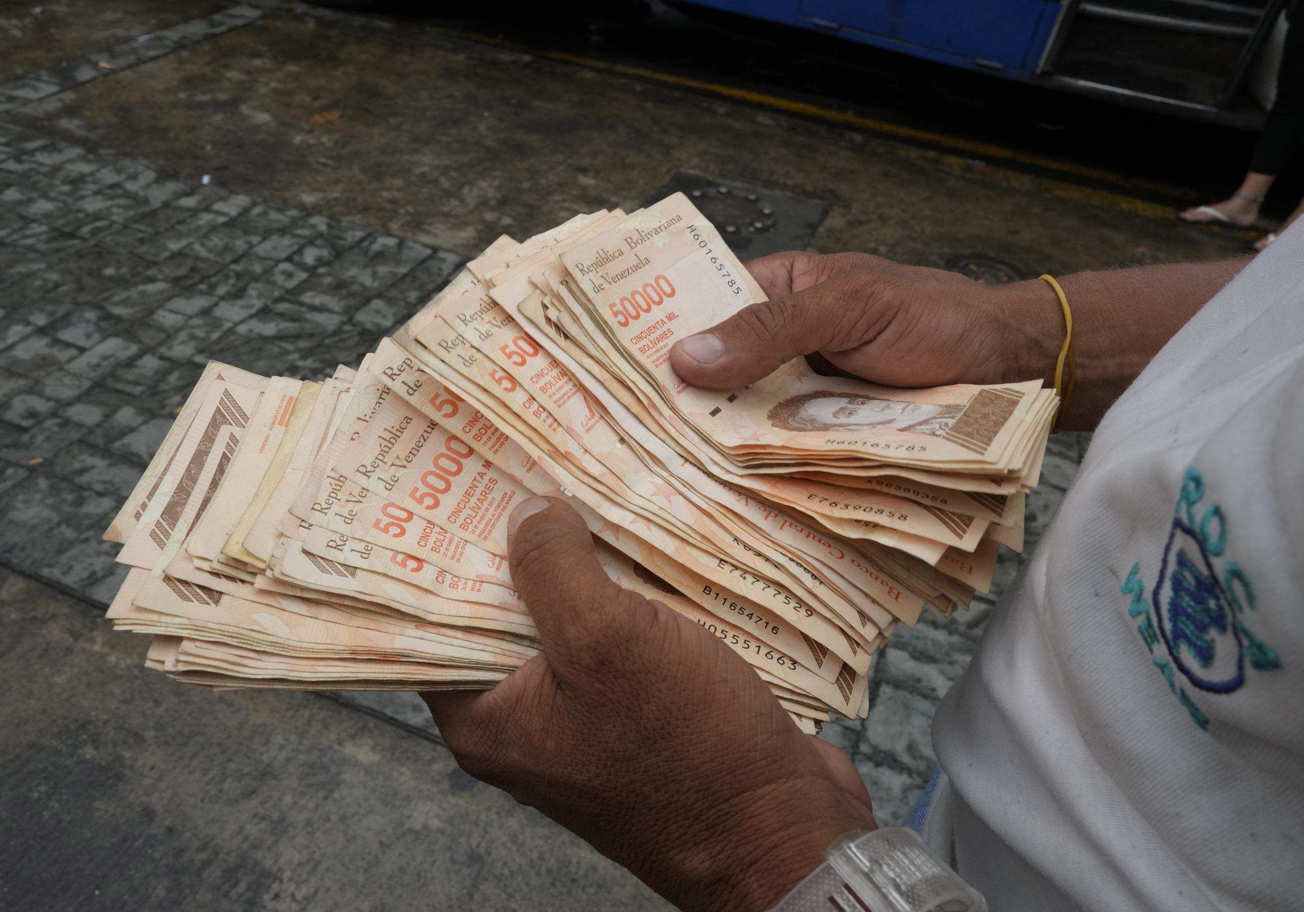 Un hombre cuenta billetes de bolívar por un valor de un dólar en una parada de autobús en Caracas, Venezuela, el jueves 5 de agosto de 2021. (AP Foto/Ariana Cubillos)