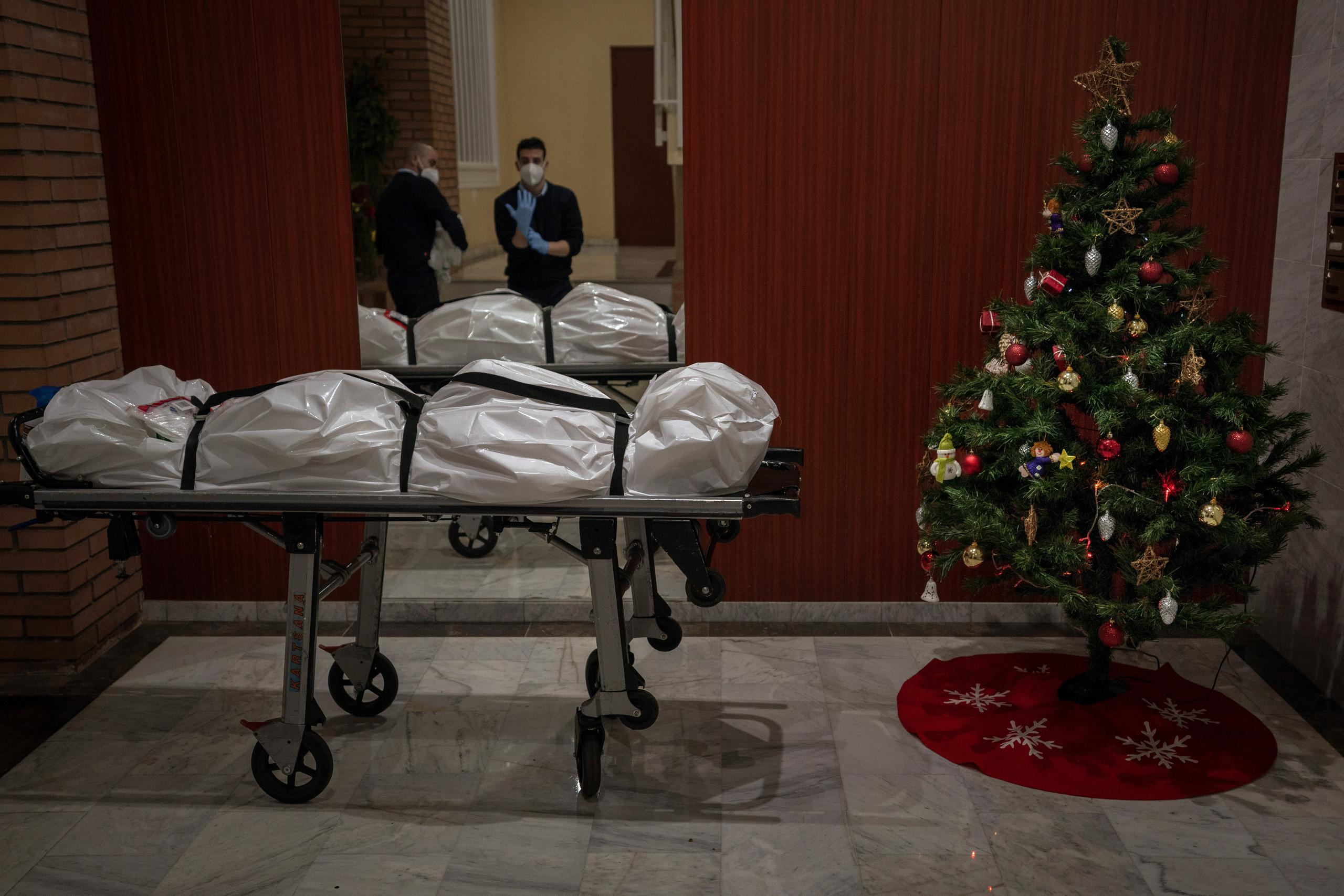 Trabajadores funerarios se quitan su ropa protectora a la entrada de un edificio decorado con un árbol de Navidad, luego de haber retirado el cuerpo de una persona que presuntamente falleció de COVID-19, en Barcelona, España.