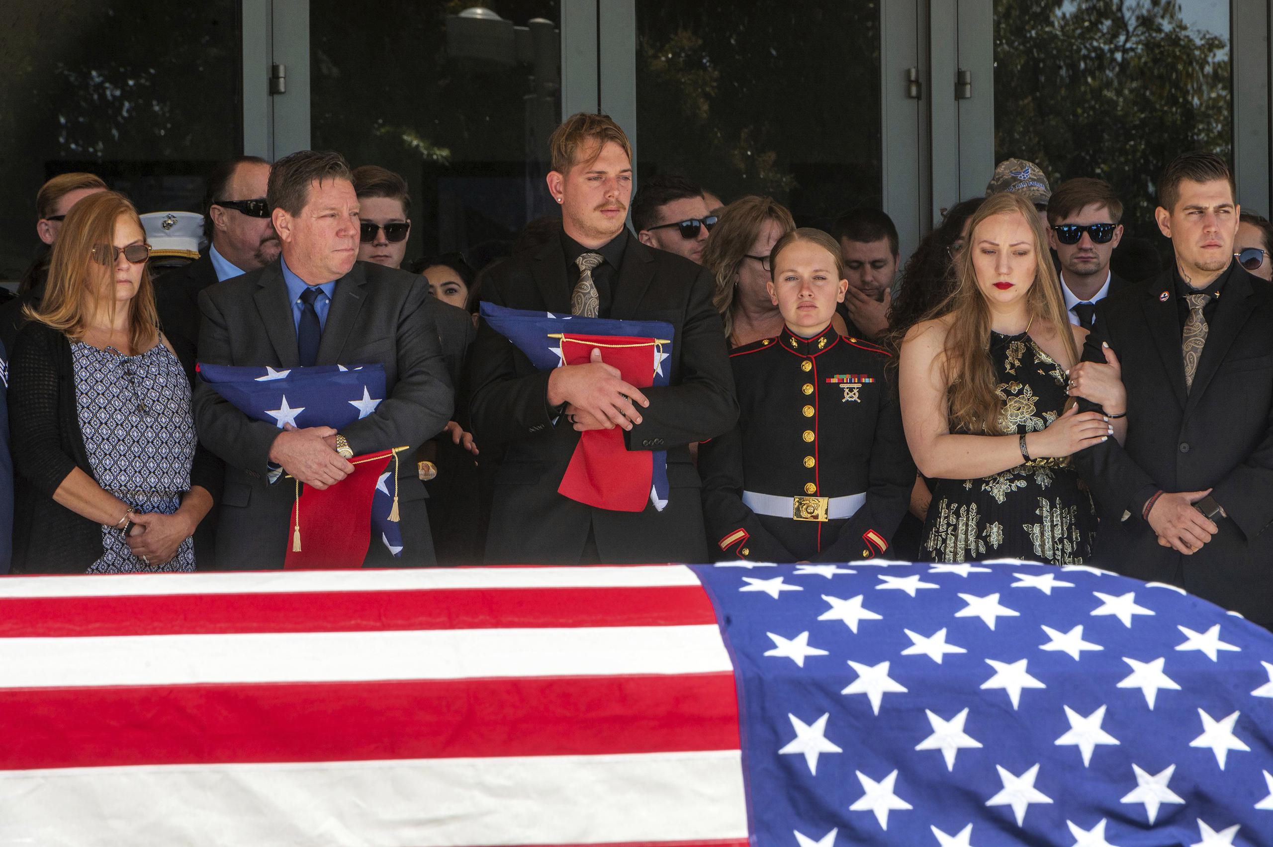 El término de un servicio religioso en memoria de la sargento de la infantería de marina Nicole Gee, cuyo féretro está envuelto en la bandera estadounidense, su padre, Richard Herrera, a la izquierda, y su esposo, Jarod Gee, sostienen banderas estadounidenses en la iglesia Bayside, en Roseville, California.