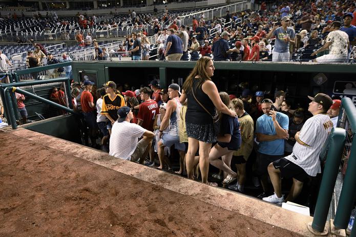 Espectadores se paran en el banquillo del equipo visitante durante una detención en el juego debido a un incidente cerca del estadio en la sexta entrada de un juego de béisbol entre los Nacionales de Washington y los Padres de San Diego.