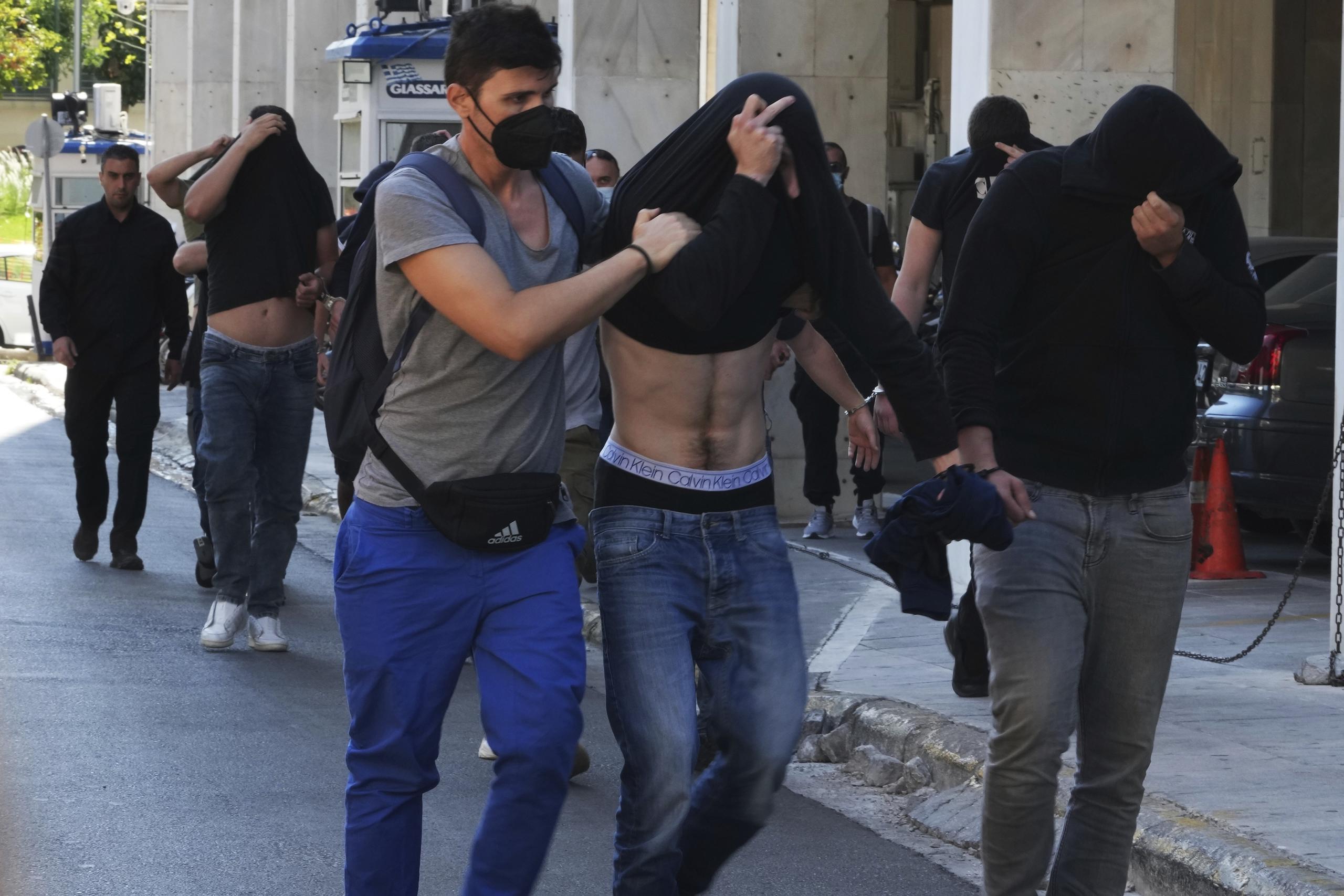 Hinchas de fútbol, en su mayoría de Croacia, se tapan los rostros, al salir del cuartel general de la policía de Atenas.