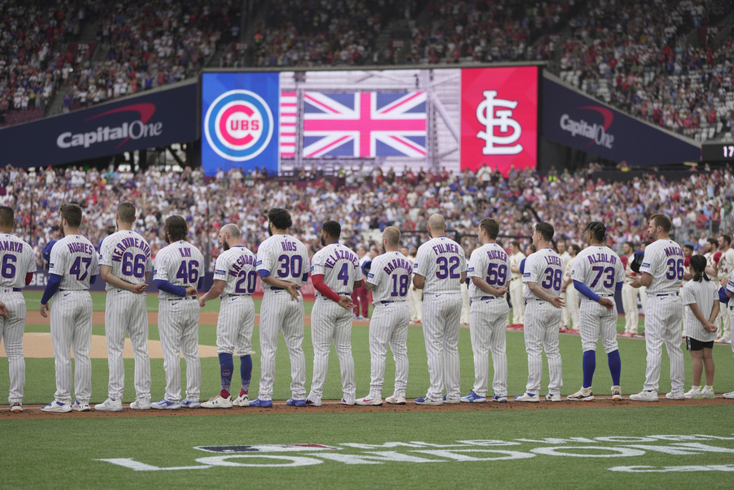 Jugadores de los Cubs de Chicago se alinean durante la ceremonia de los himnos de Estados Unidos e Inglaterra previo al partido de béisbol en contra de los Cardinals de San Luis.
