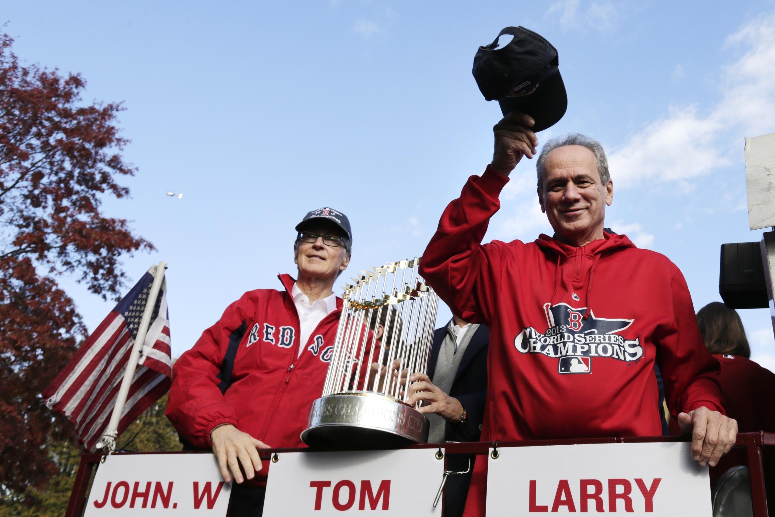 El presidente de los Red Sox de Boston en el 2013 lo era Larry Lucchino, quien aparece a la derecha saludando a los fanáticos junto al dueño John Henry durante el desfile de celebración por la consagración en la Serie Mundial de ese año.