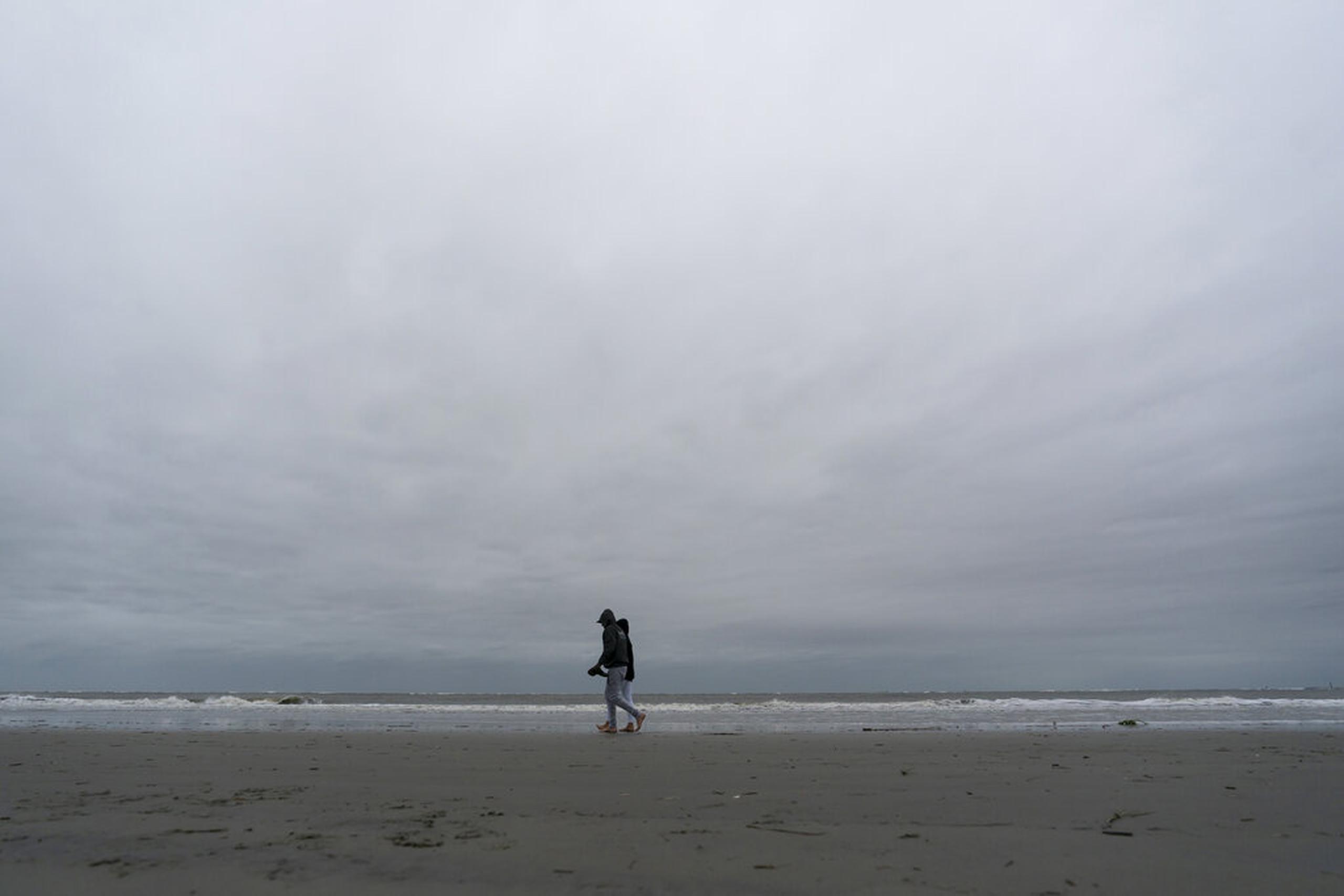 Gente camina por la playa durante la marea baja mientras se sienten los efectos del huracán Ian, el 29 de septiembre de 2022, en Sullivan's Island, Carolina del Sur.