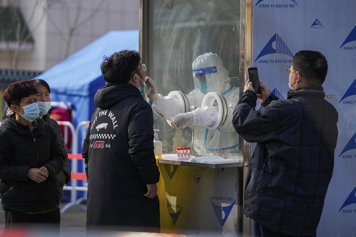 Un hombre usa un teléfono celular para fotografiar a los vecinos que reciben un hisopado de garganta en un sitio de pruebas para el coronavirus en el distrito Xichen de Beijing, martes 25 de enero de 2022.
