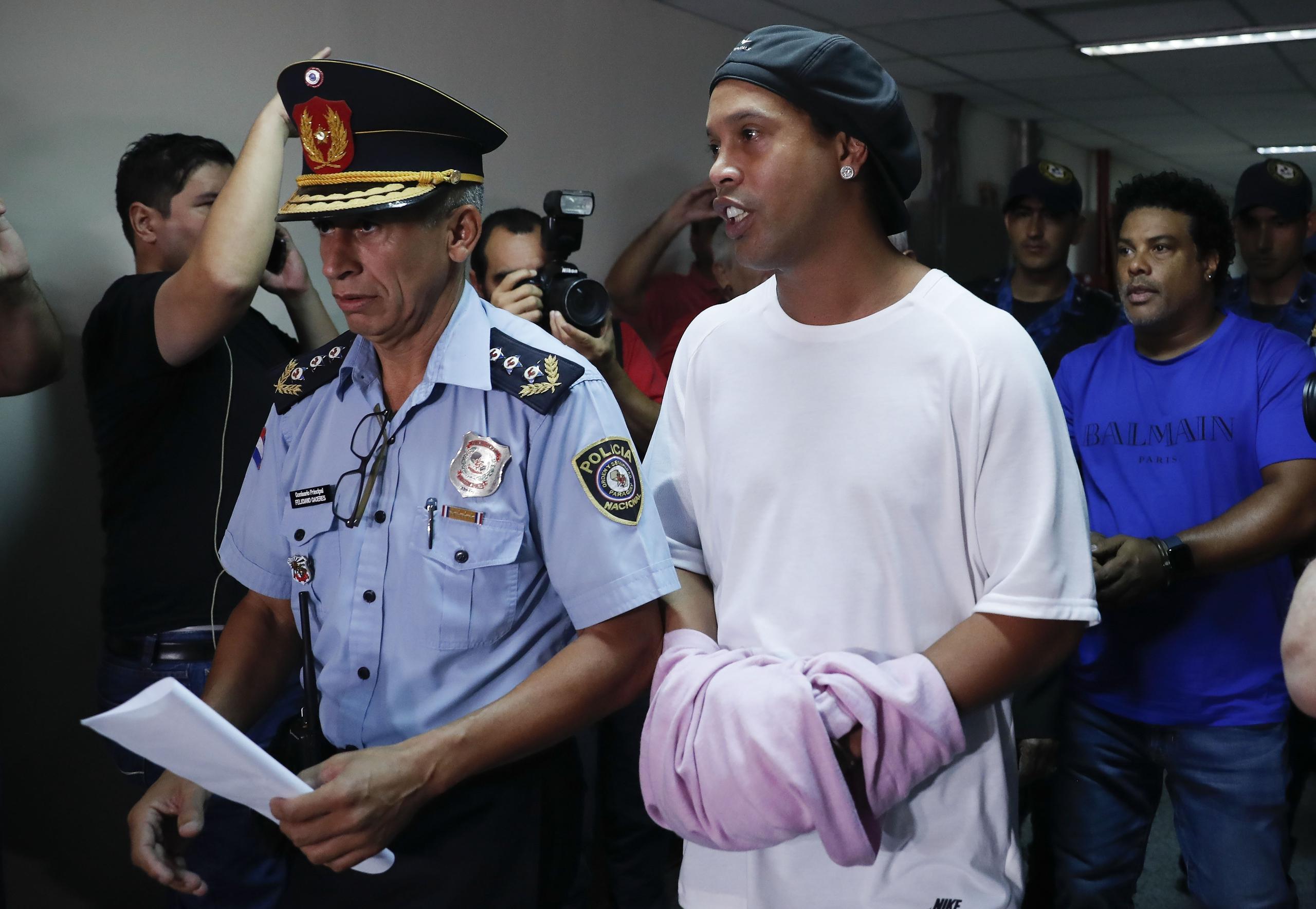 El exastro brasileño de fútbol Ronaldinho camina esposado a una audiencia judicial en Asunción, Paraguay, el sábado, 27  de marzo del 2020.