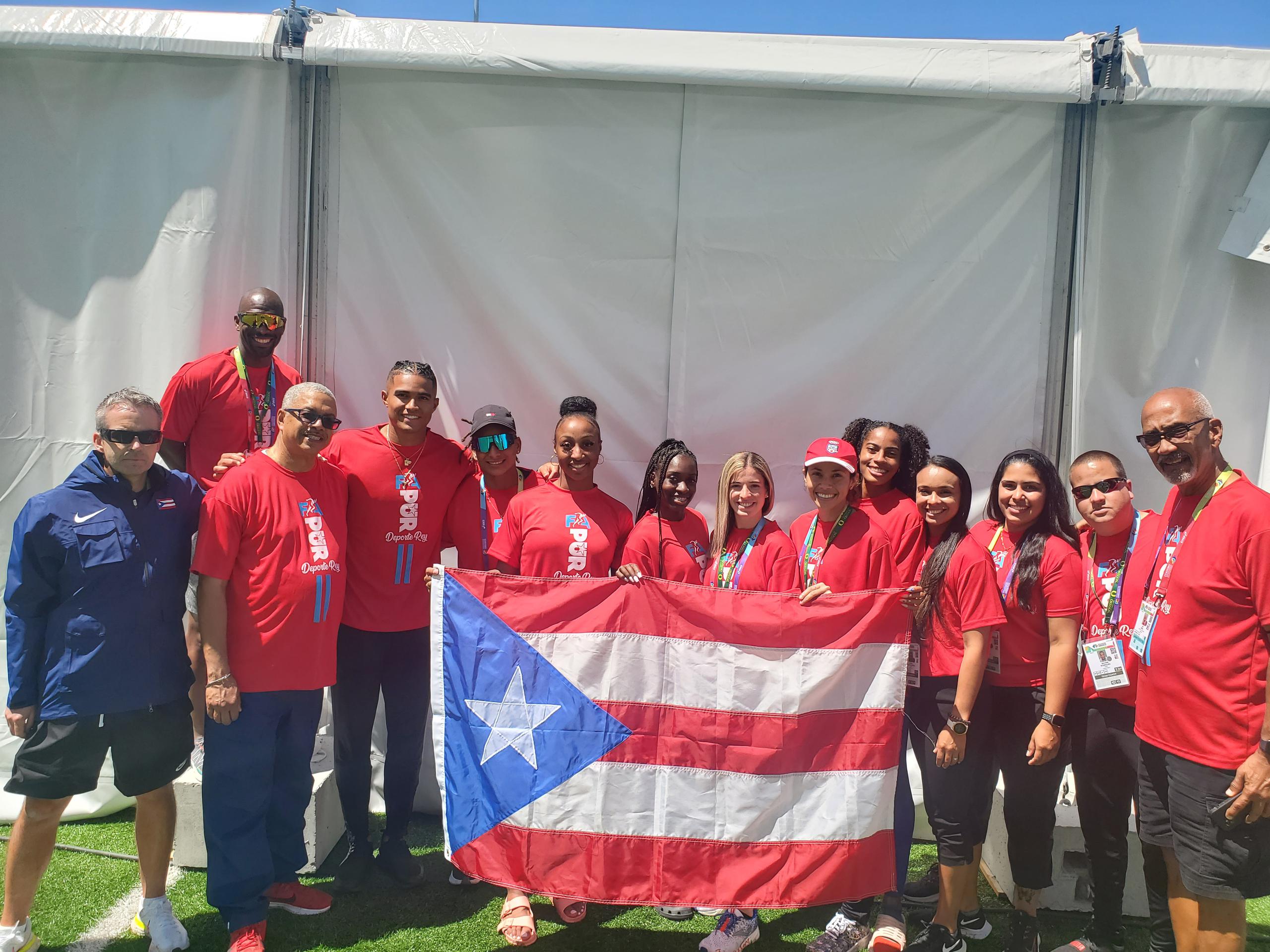 La delegación de Puerto Rico, incluyendo a la campeona olímpica Jasmine Camacho-Quinn, posa con la bandera boricua.