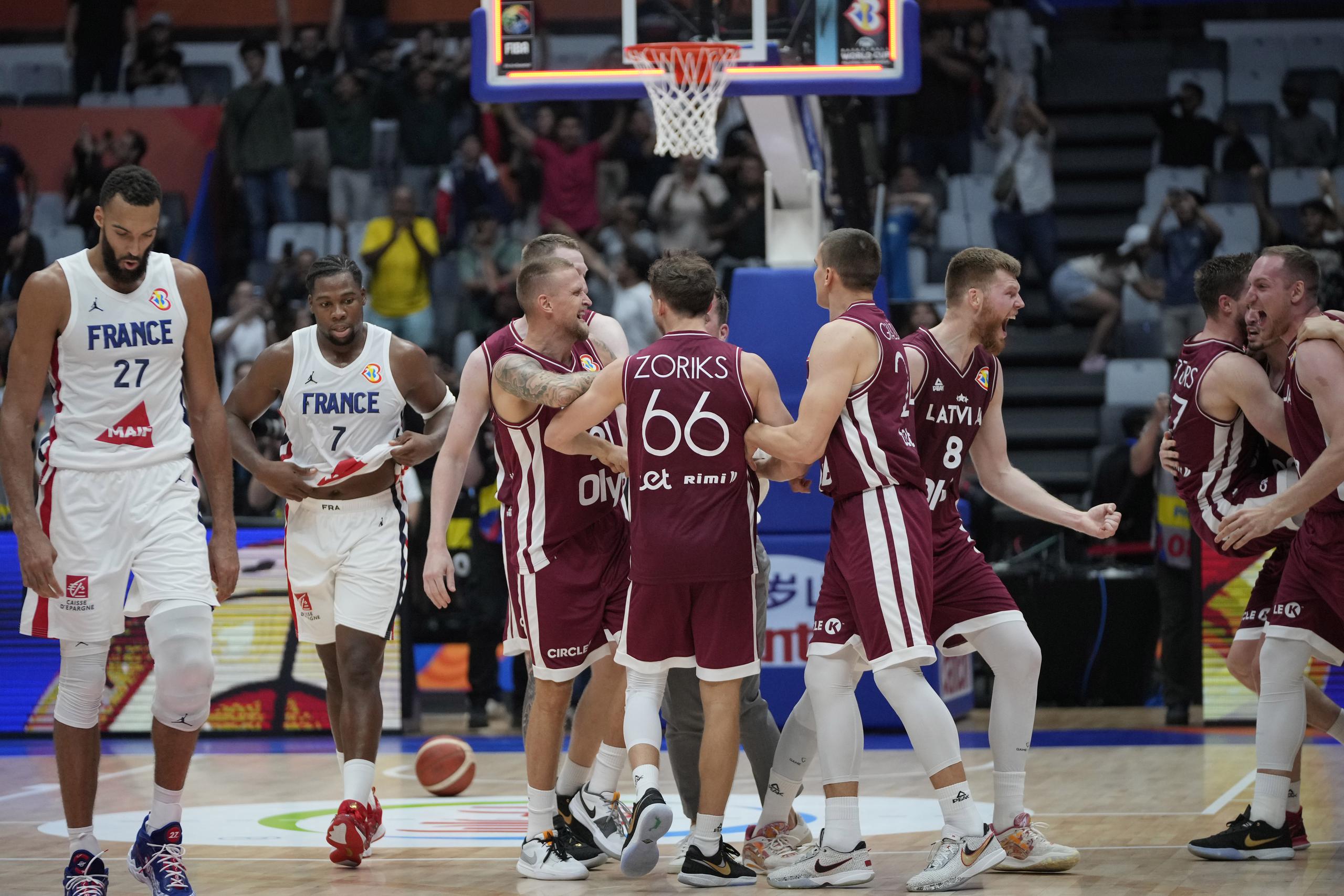 Los jugadores de Letonia celebran mientras dos canasteros de Francia comienza su agónica caminata hacia el camerino luego de sucumbir ante ellos para quedar sin opciones de clasificación a la segunda ronda de la Copa del Mundo.