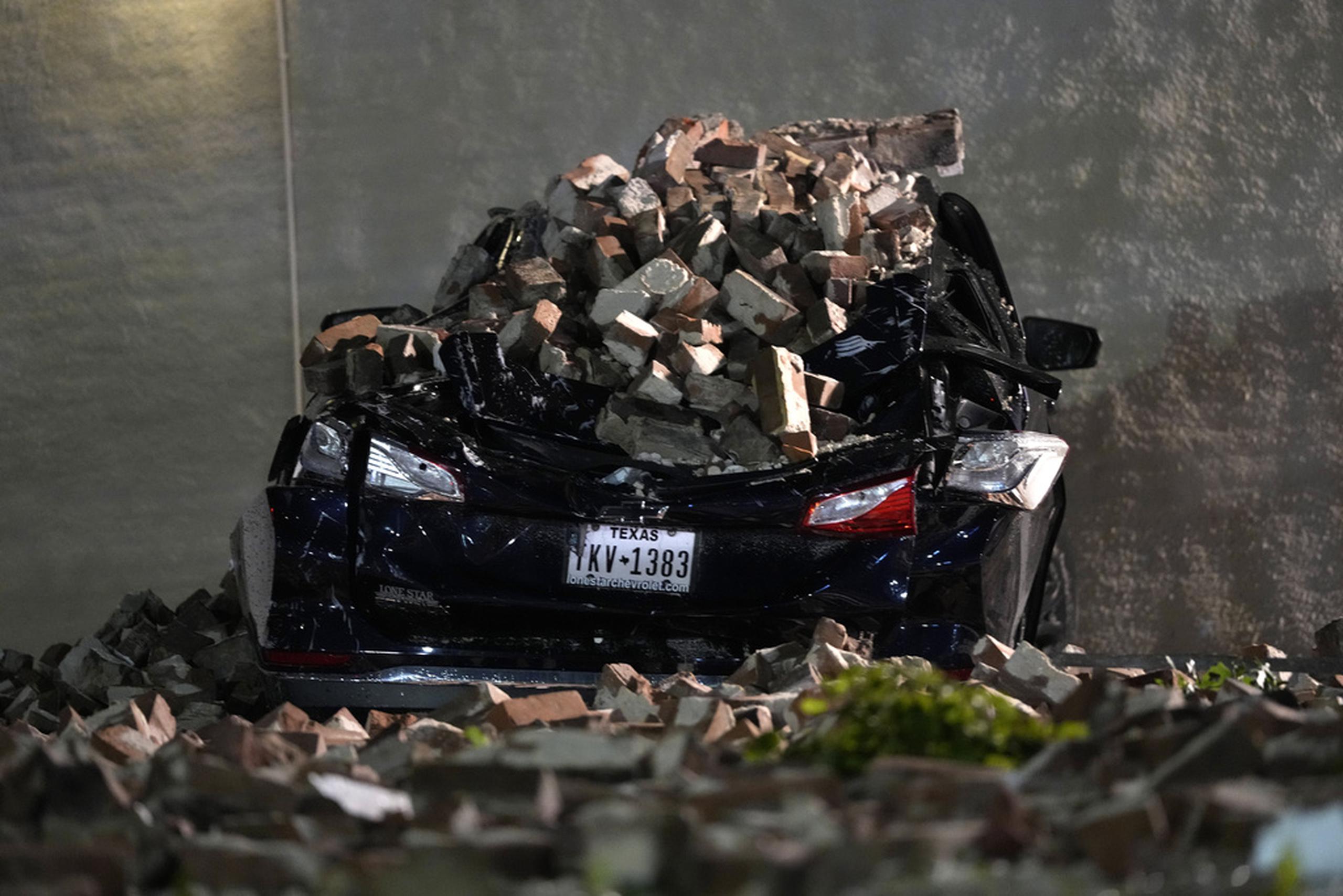Un automóvil aplastado por ladrillos desprendidos del muro de un edificio yace en un estacionamiento del centro de Houston.