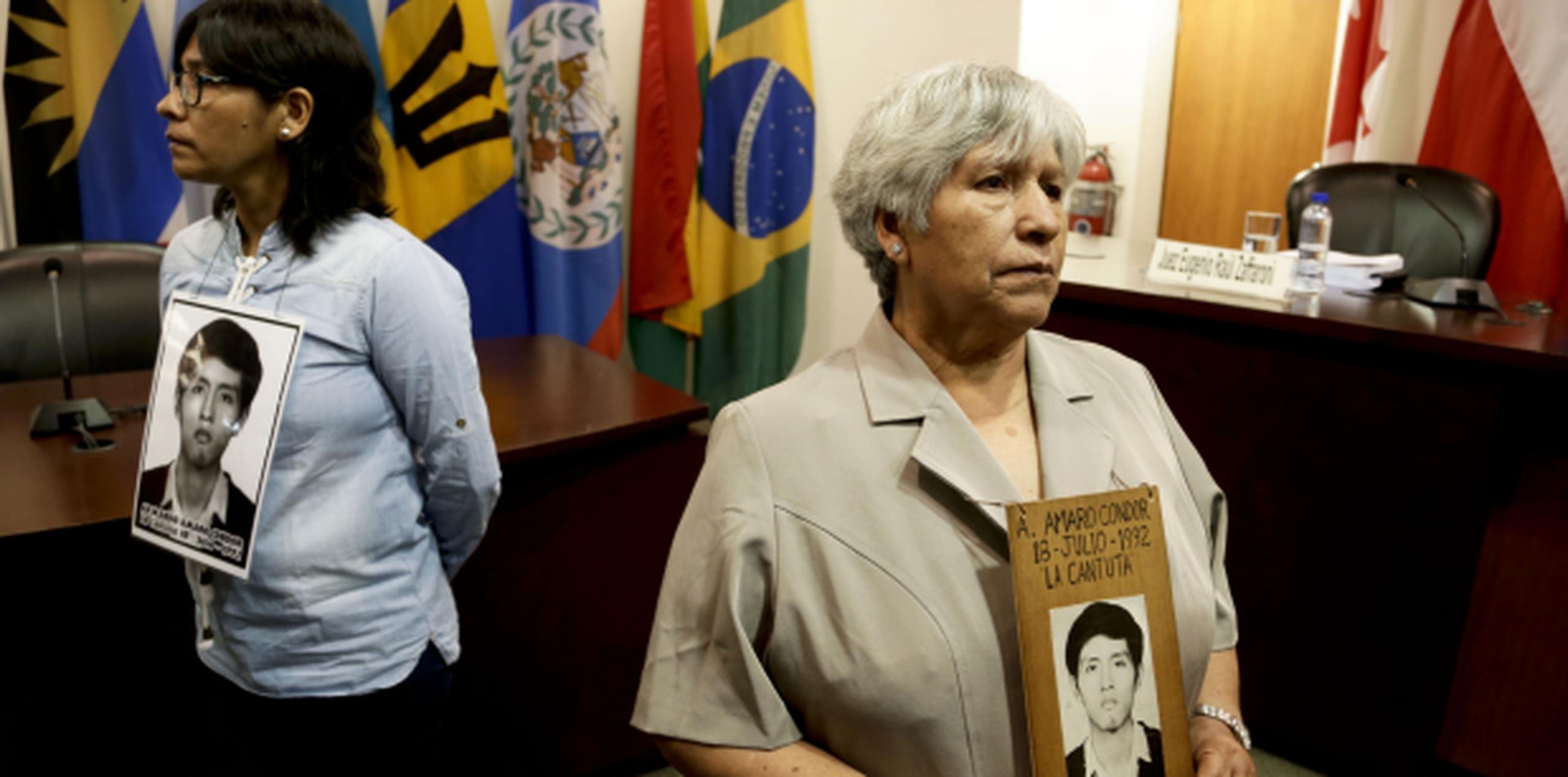 Dos mujeres llevan en una sala judicial el retrato de una de las personas asesinadas que le imputan al expresidente Alberto Fujimori. (AP)