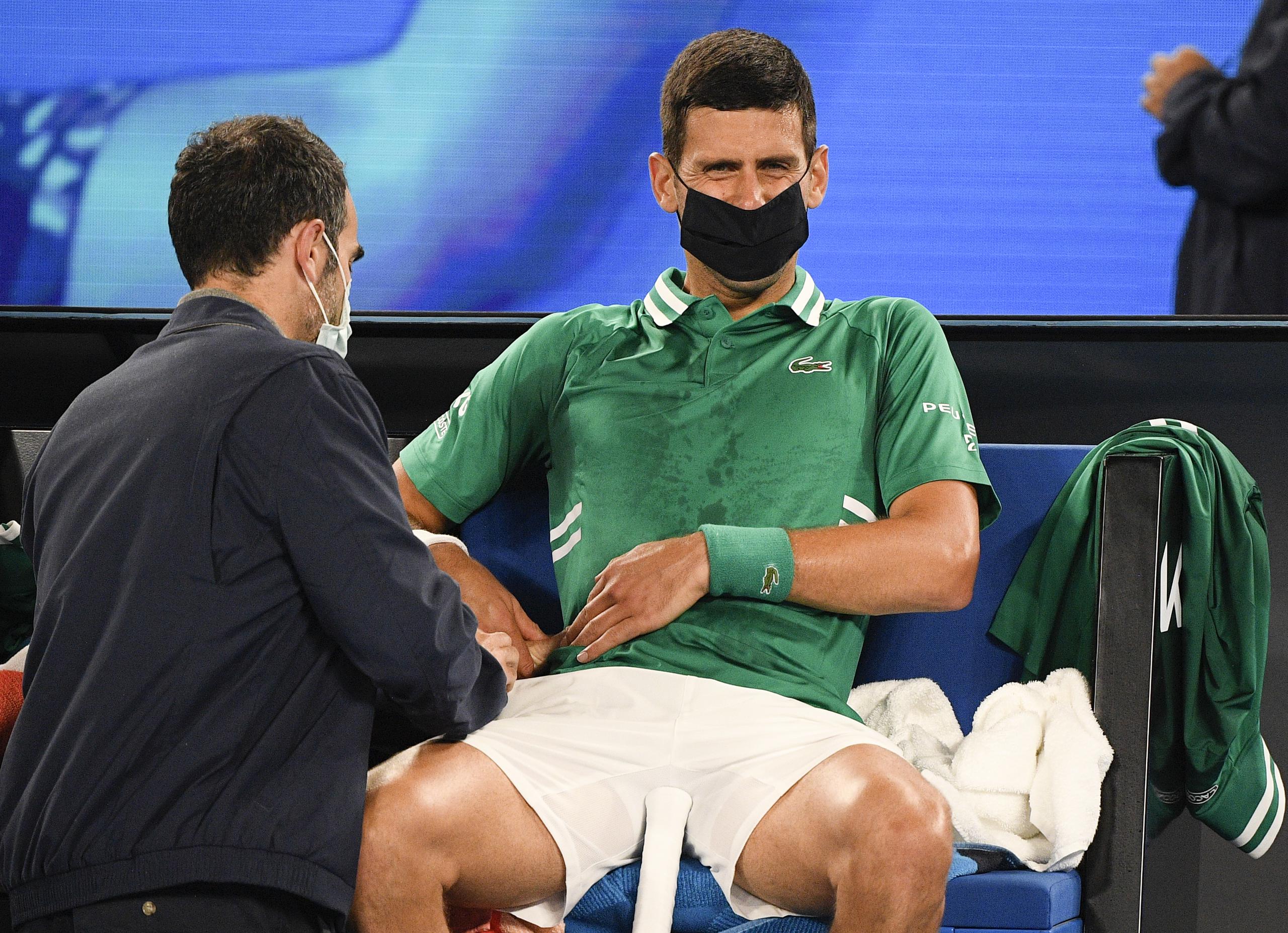 Novak Djokovic recibe atención médica mientras se toca el área resentida.
