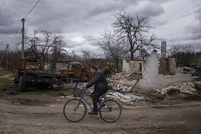 Un hombre anda en bicicleta frente a vehículos y un edificio destrozados en Yahidne, Ucrania, el 12 de abril de 2022.
