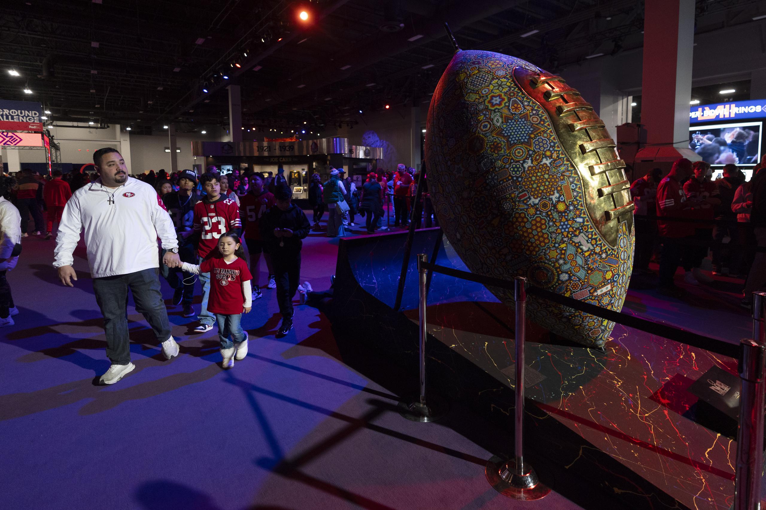 Aficionados caminan junto a una escultura de un balón de fútbol americano decorado en el NFL Experience en Las Vegas antes del Super Bowl 58 en Las Vegas.