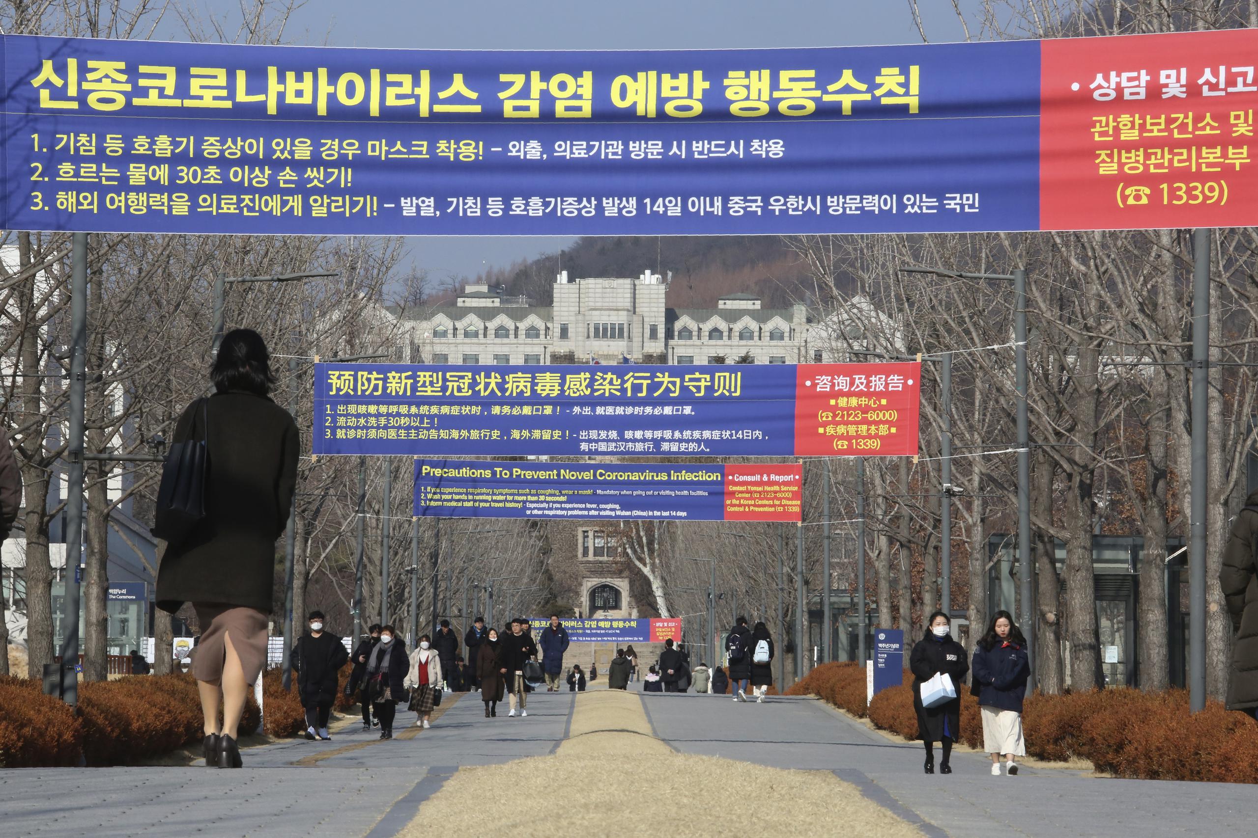Varias personas caminan por debajo de carteles que informan sobre las precauciones sobre un nuevo coronavirus, en la Universidad Yeonsei de Seúl, Corea del Sur.
