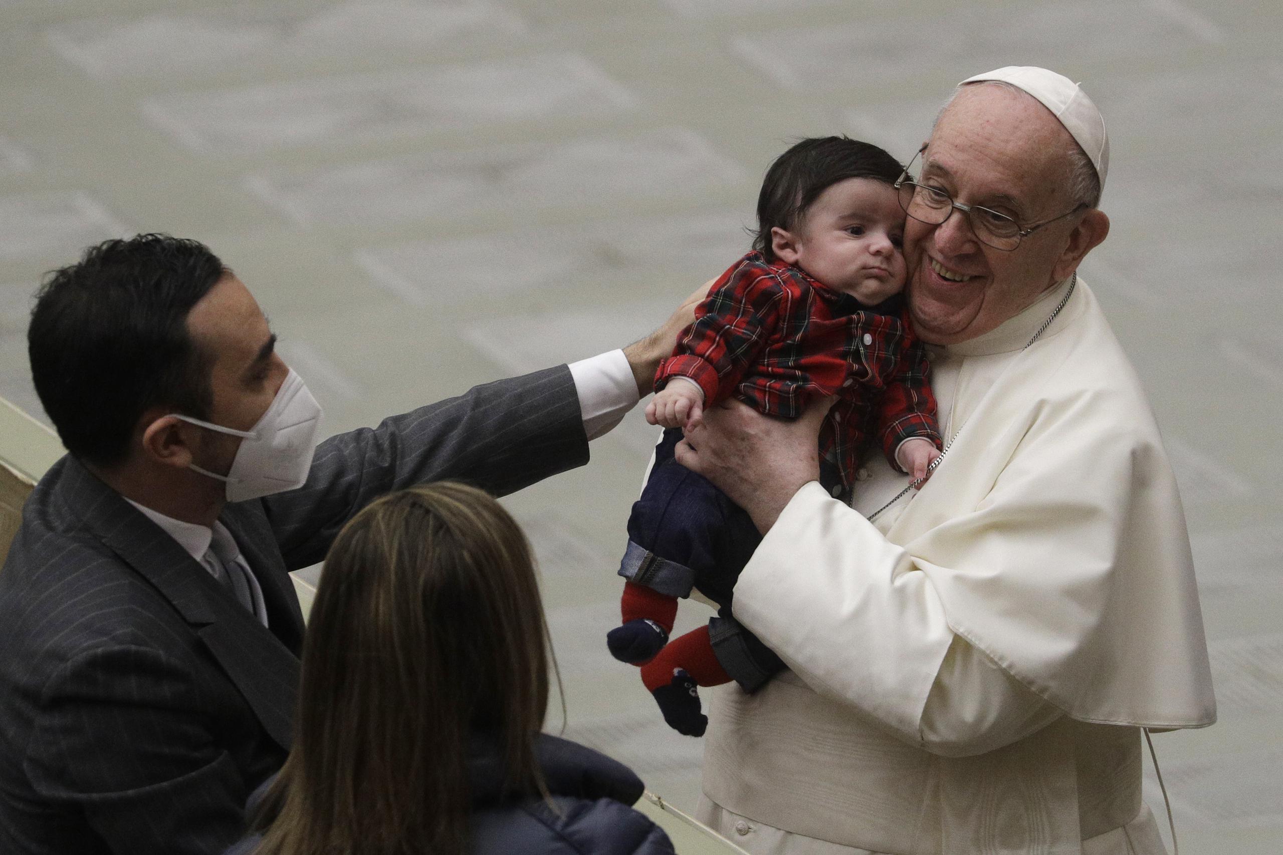El papa Francisco carga un bebé mientras intercambia buenos deseos navideños con empleados del Vaticano en el salón Paulo VI.