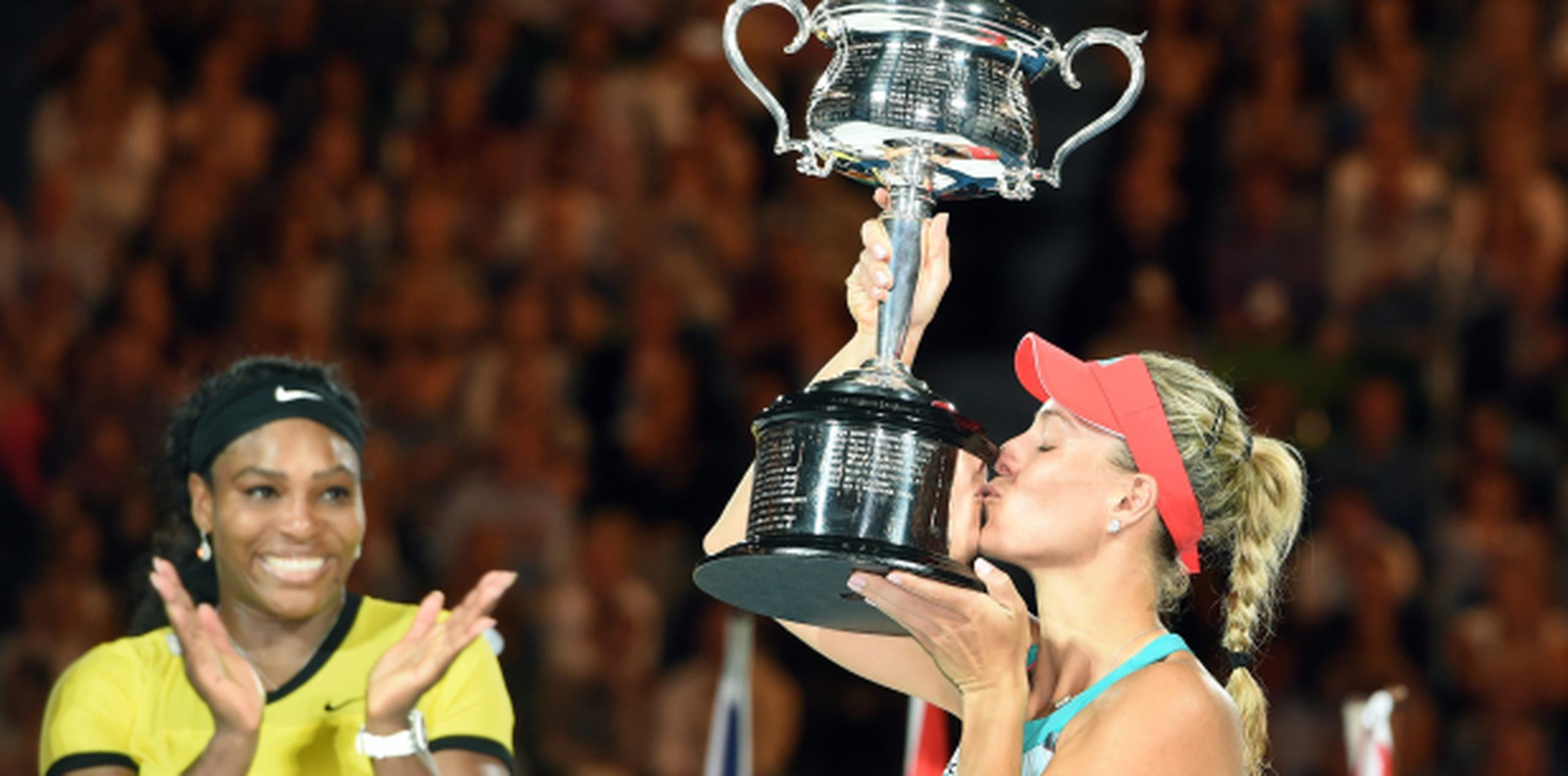La alemana Angelique Kerber besa el trofeo que obtuvo al vencer a Serena Williams quien aplaude en reconocimiento al triunfo de su rival. (EFE)