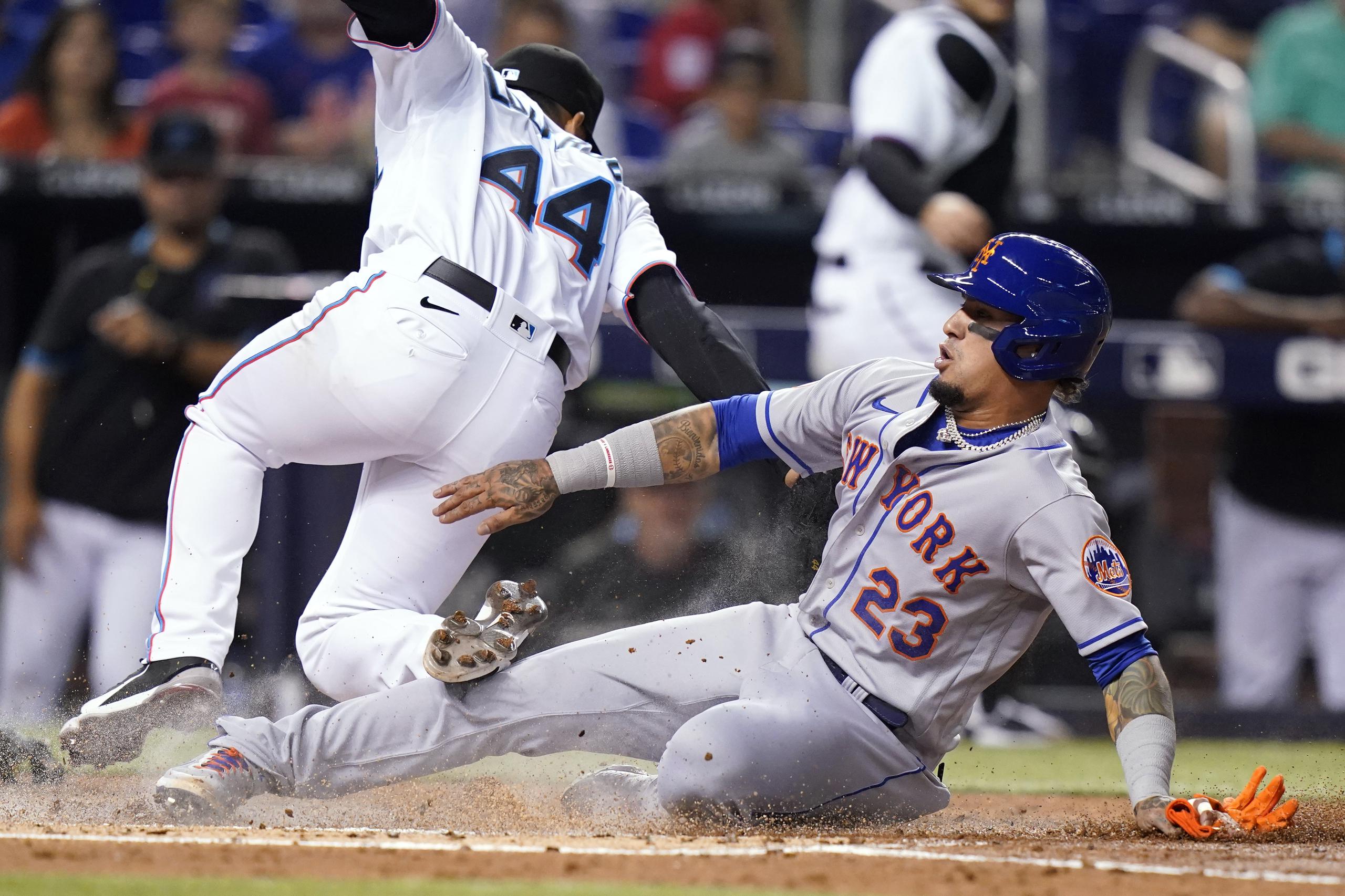 Javier Báez, de los Mets de Nueva York, se desliza en el plato al anotar desde tercera base con un lanzamiento salvaje del lanzador Jesús Luzardo (44), quien cubre el plato.