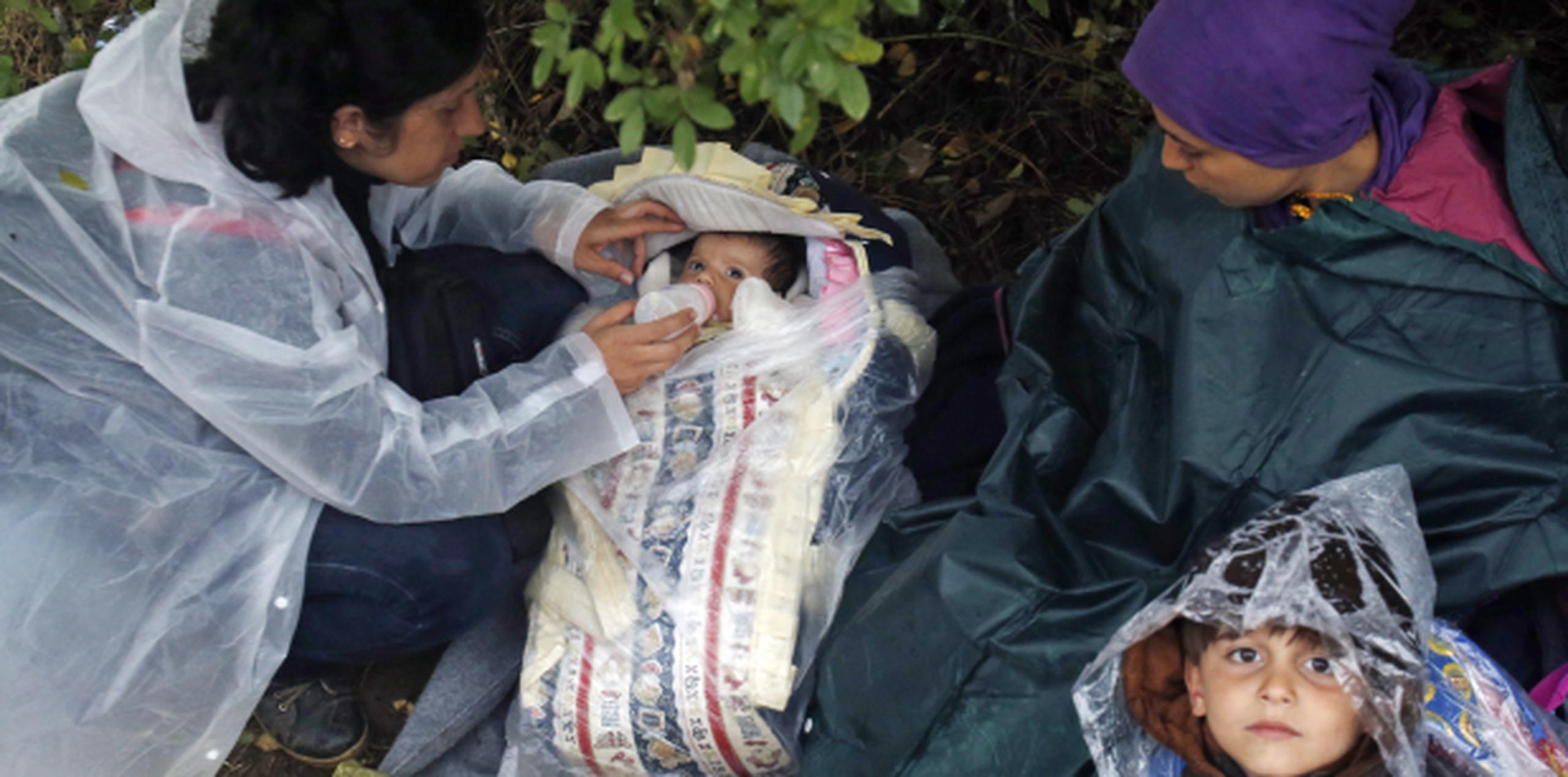 Usando capas para la lluvia, una mujer alimenta a un bebé mintras una niña inmigrante mira fijamente. (AP)