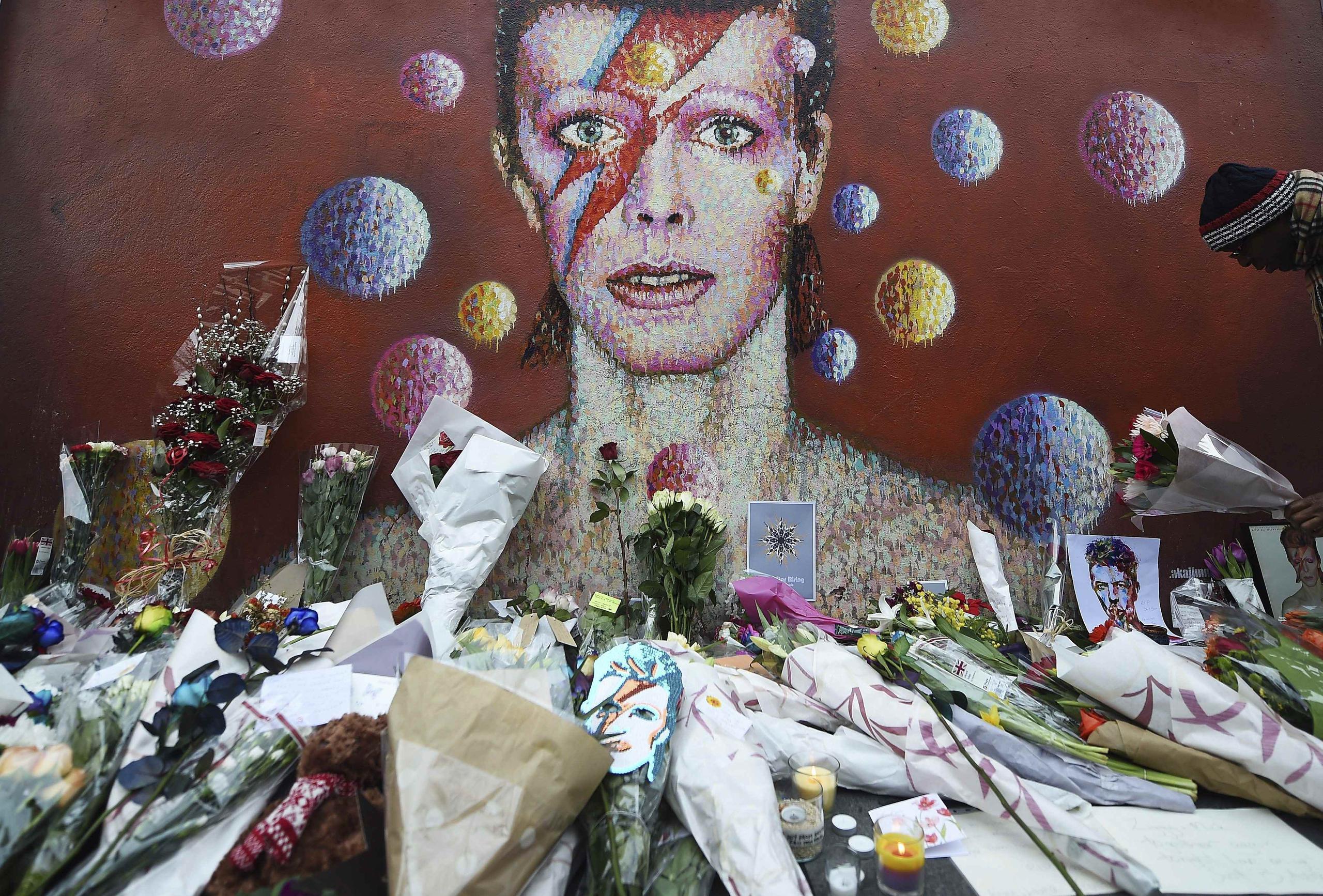 Flores y velas depositadas por los fans junto a un mural del cantante británico David Bowie en su ciudad natal en en Brixton, Londres. (EFE)