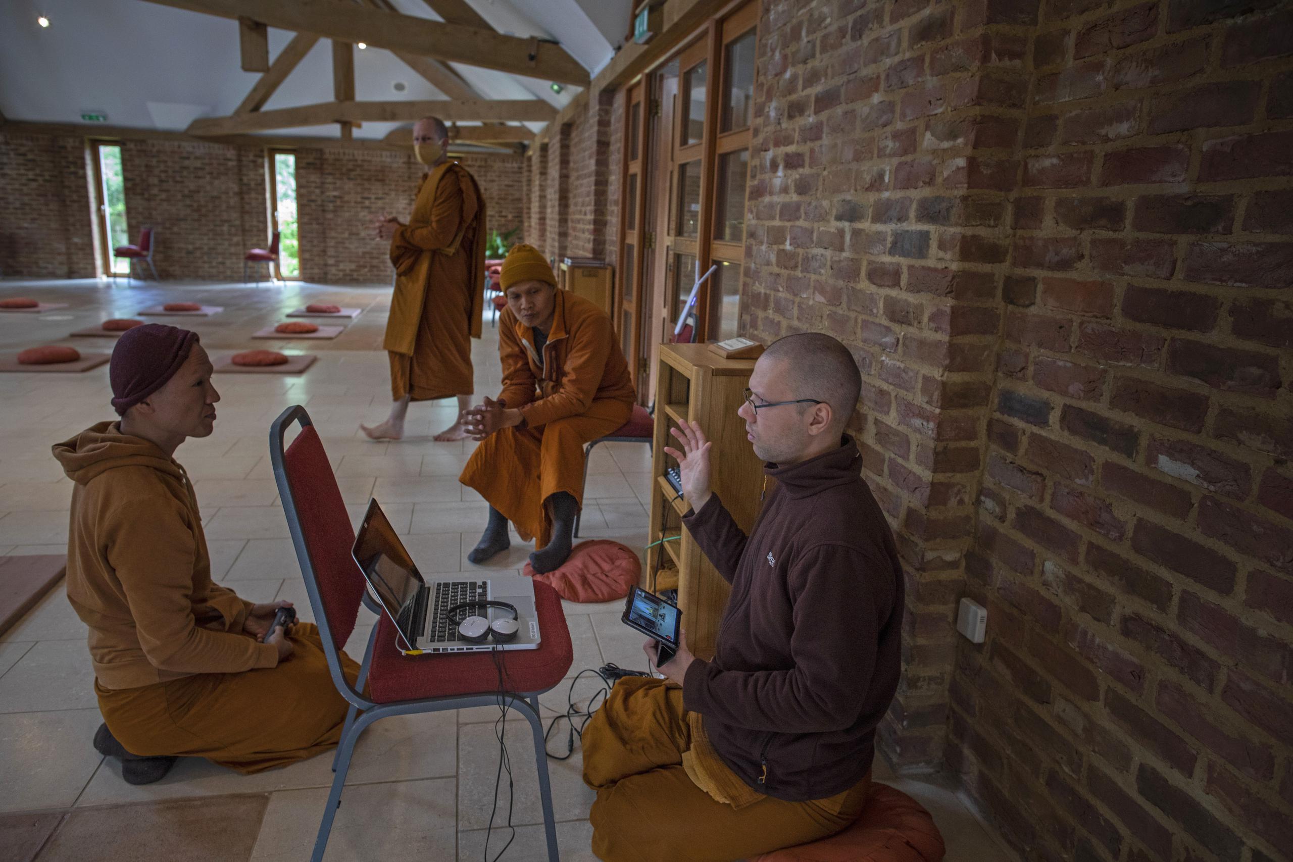 Los monjes Ajahn Kongrit, derecha, Tan Jalito, izquierda, y Tan Narindo analizan la logística del streaming en vivo de la ceremonia del Día de la Luna desde el templo budista Amvrati cerrado al público debido a la pandemia, en Great Gaddesden, Inglaterra